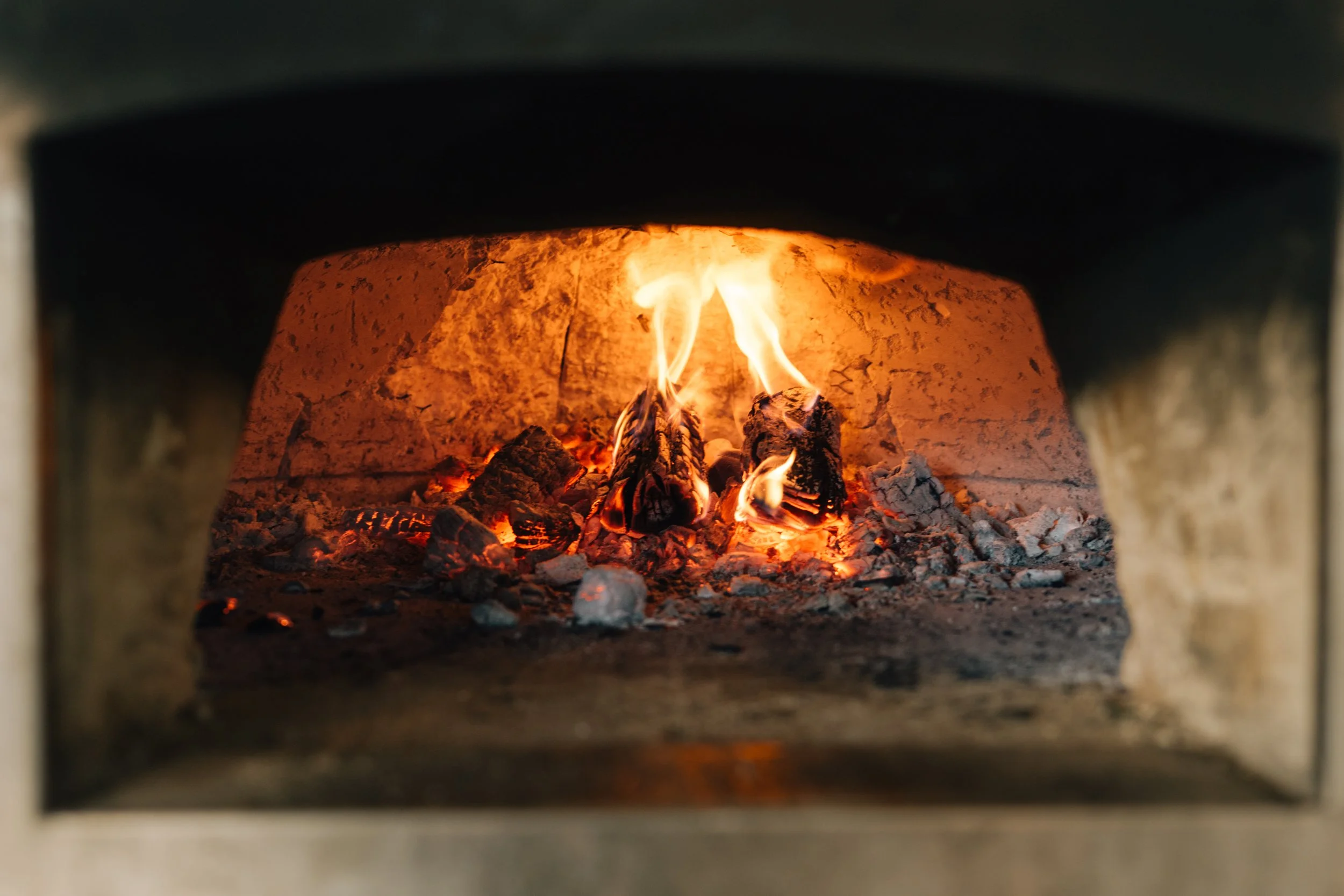 Inside a brick oven with glowing ashes and burning logs