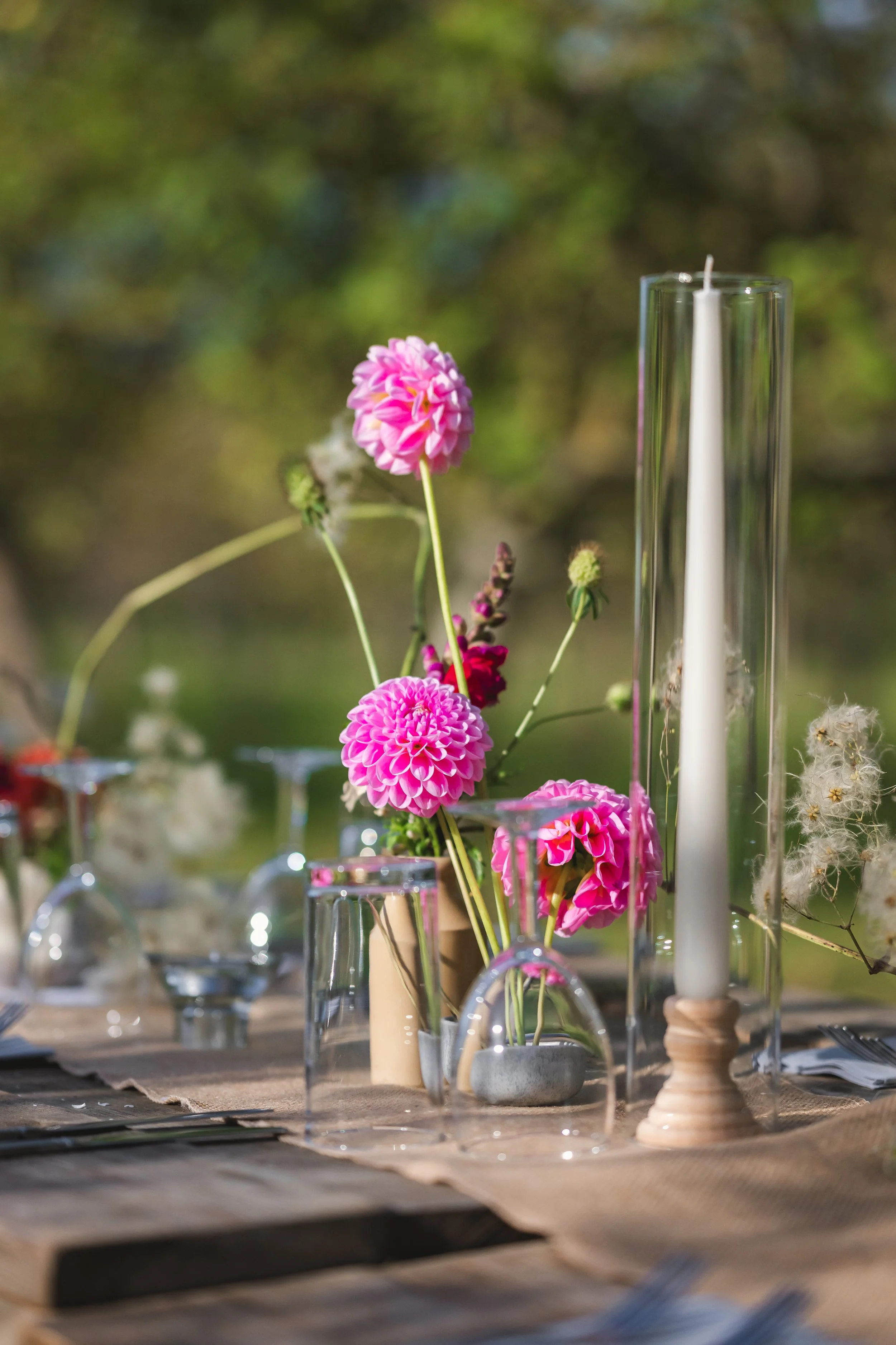 Table decorated with pink flowers in vases and candles, set outdoors