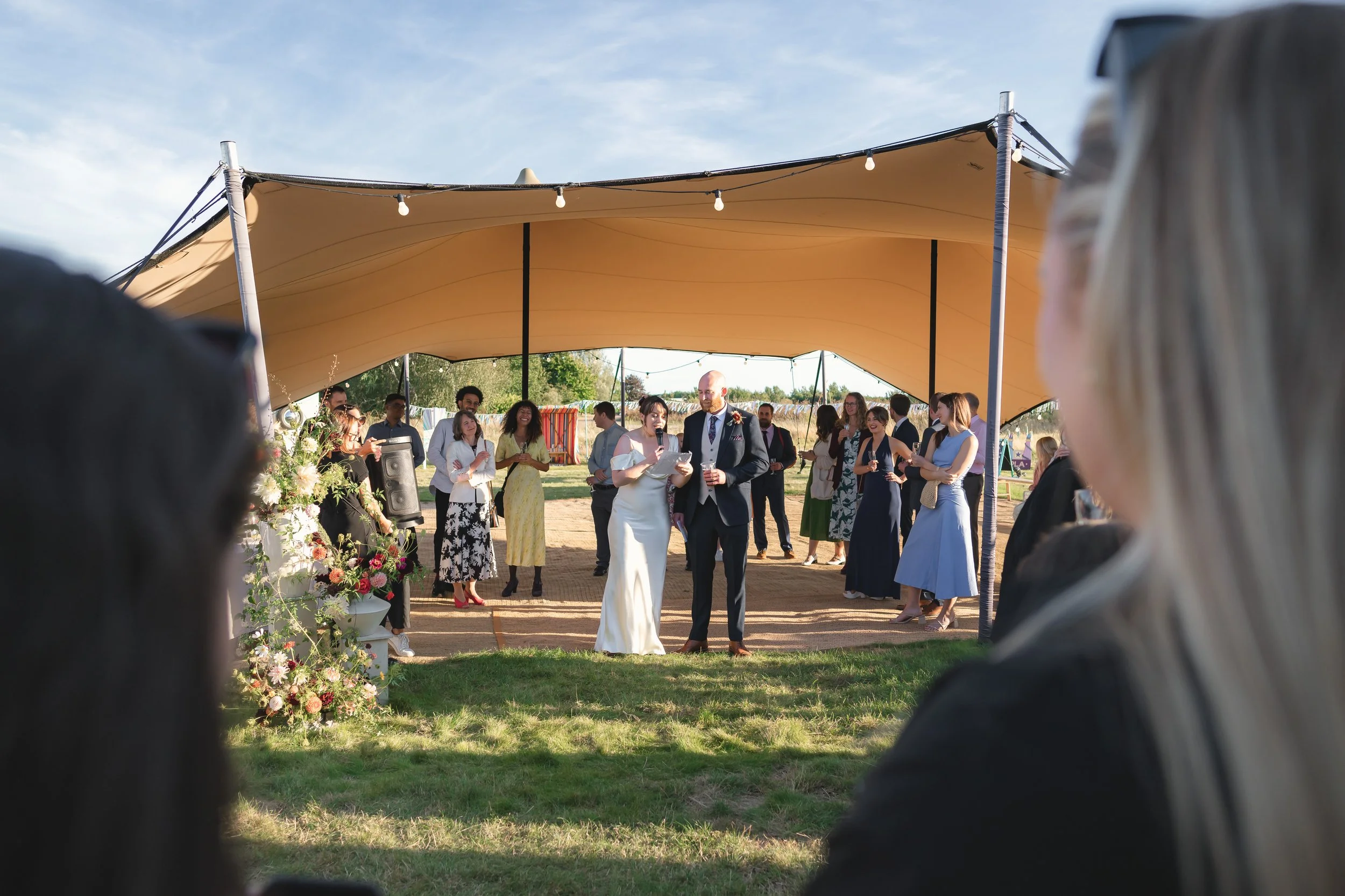 Outdoor wedding ceremony with a bride and groom standing under a canopy, surrounded by guests.