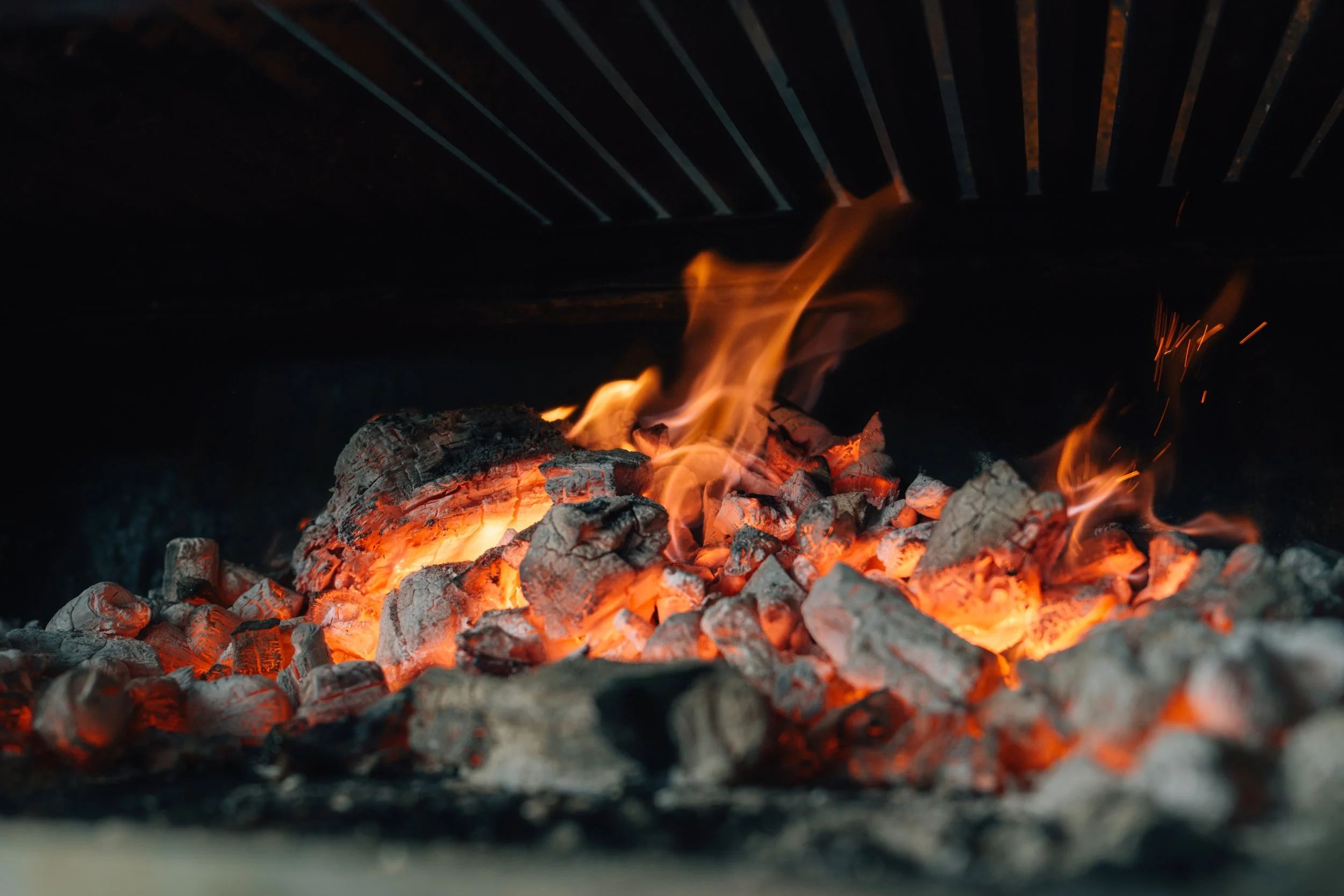 Close-up of glowing hot embers and flames inside a barbecue grill.