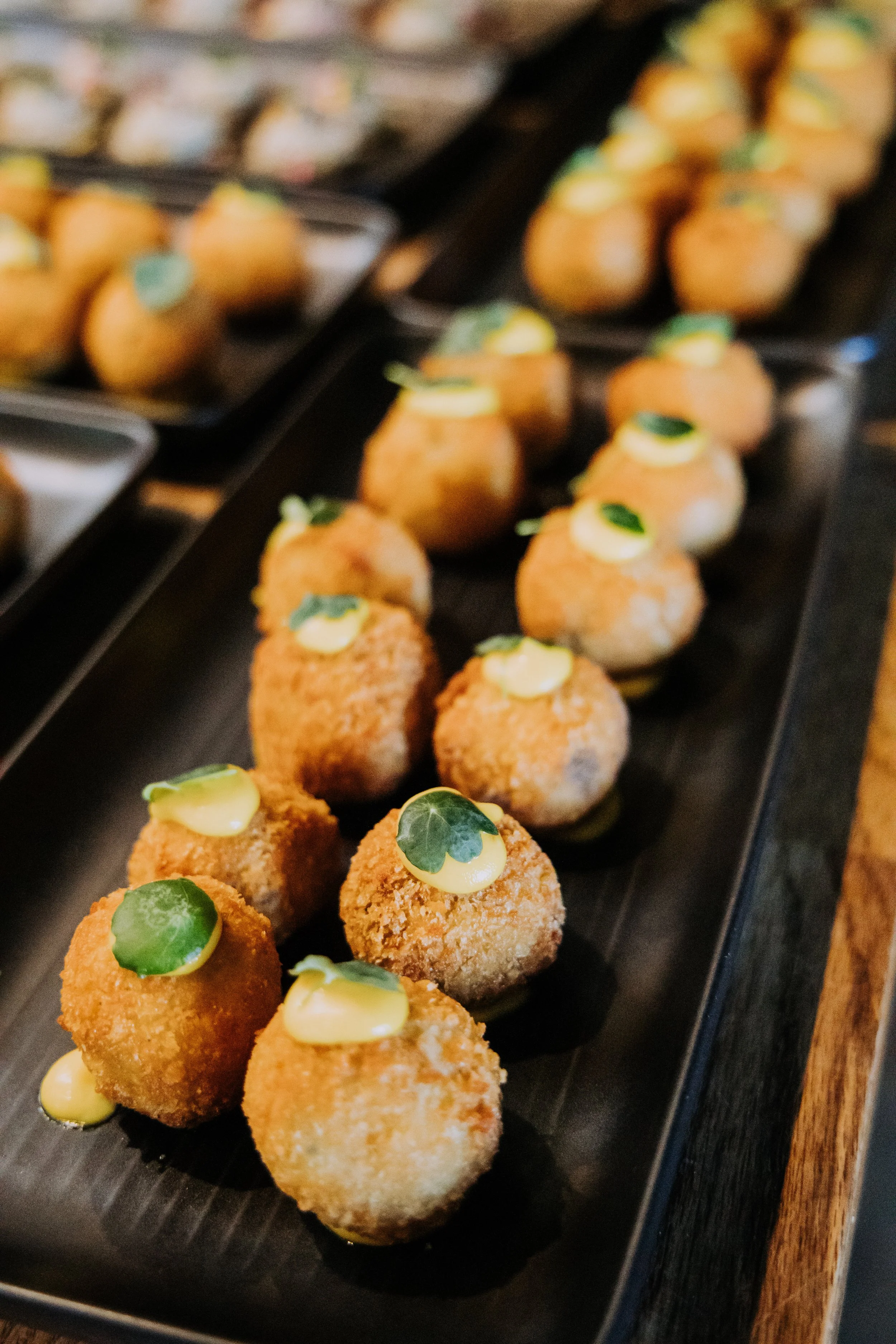A tray of breaded and fried appetizer balls topped with a dollop of yellow sauce and a small green herb leaf.