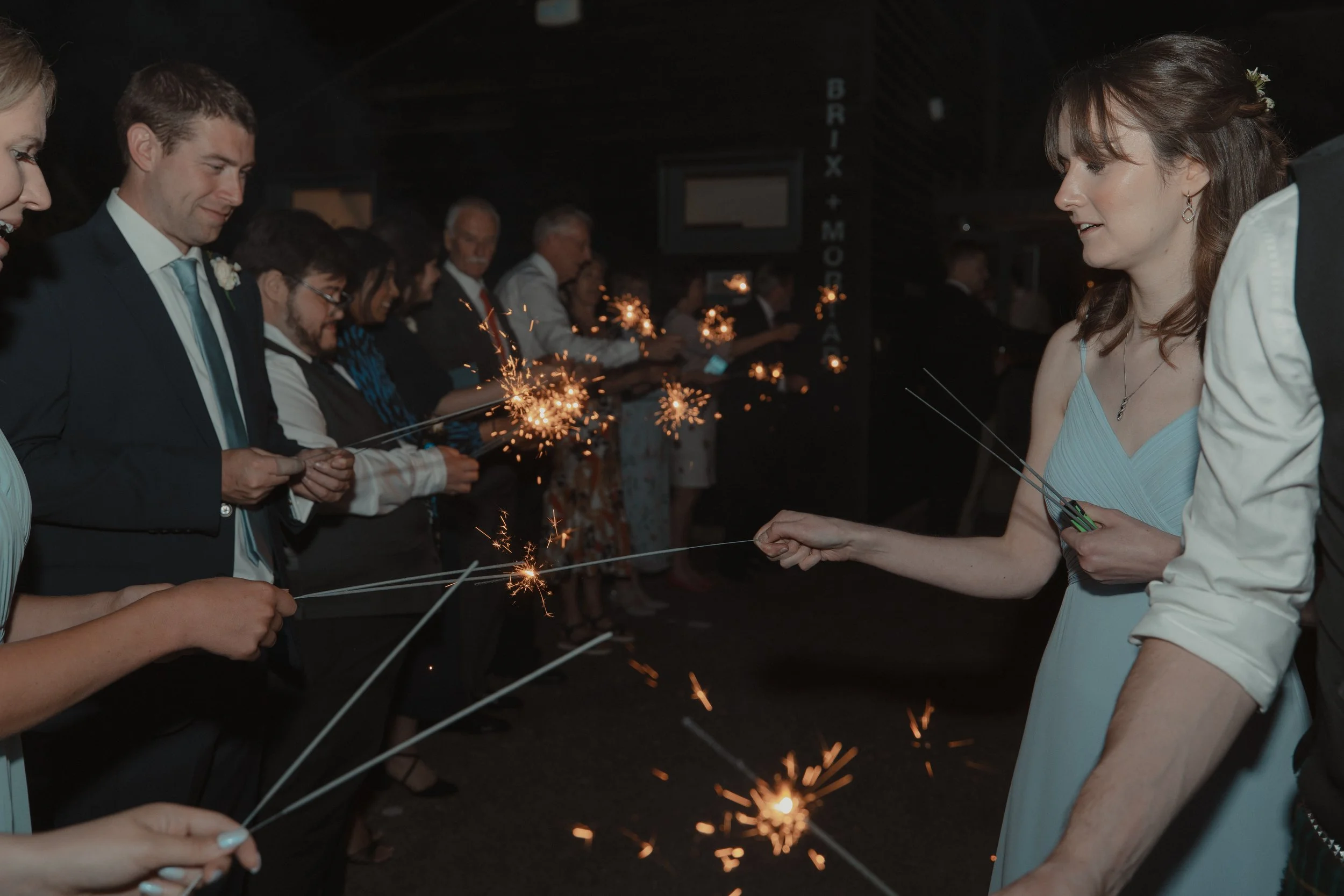 People dressed in formal clothing celebrating with sparklers at night during a festive event or party.