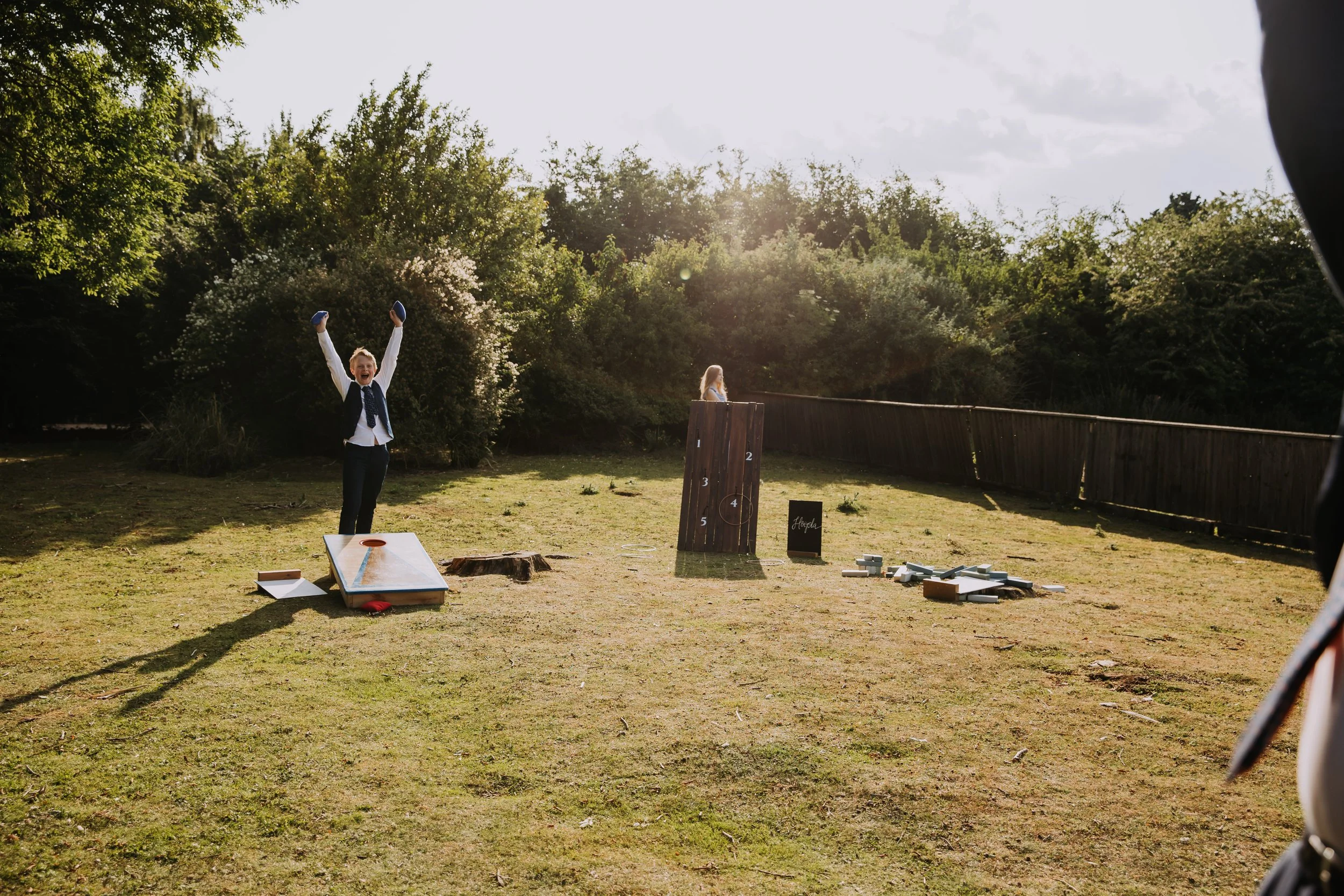 Child celebrating after playing mini-golf outdoors on a sunny day with various game setups and a wooden fence in the background.