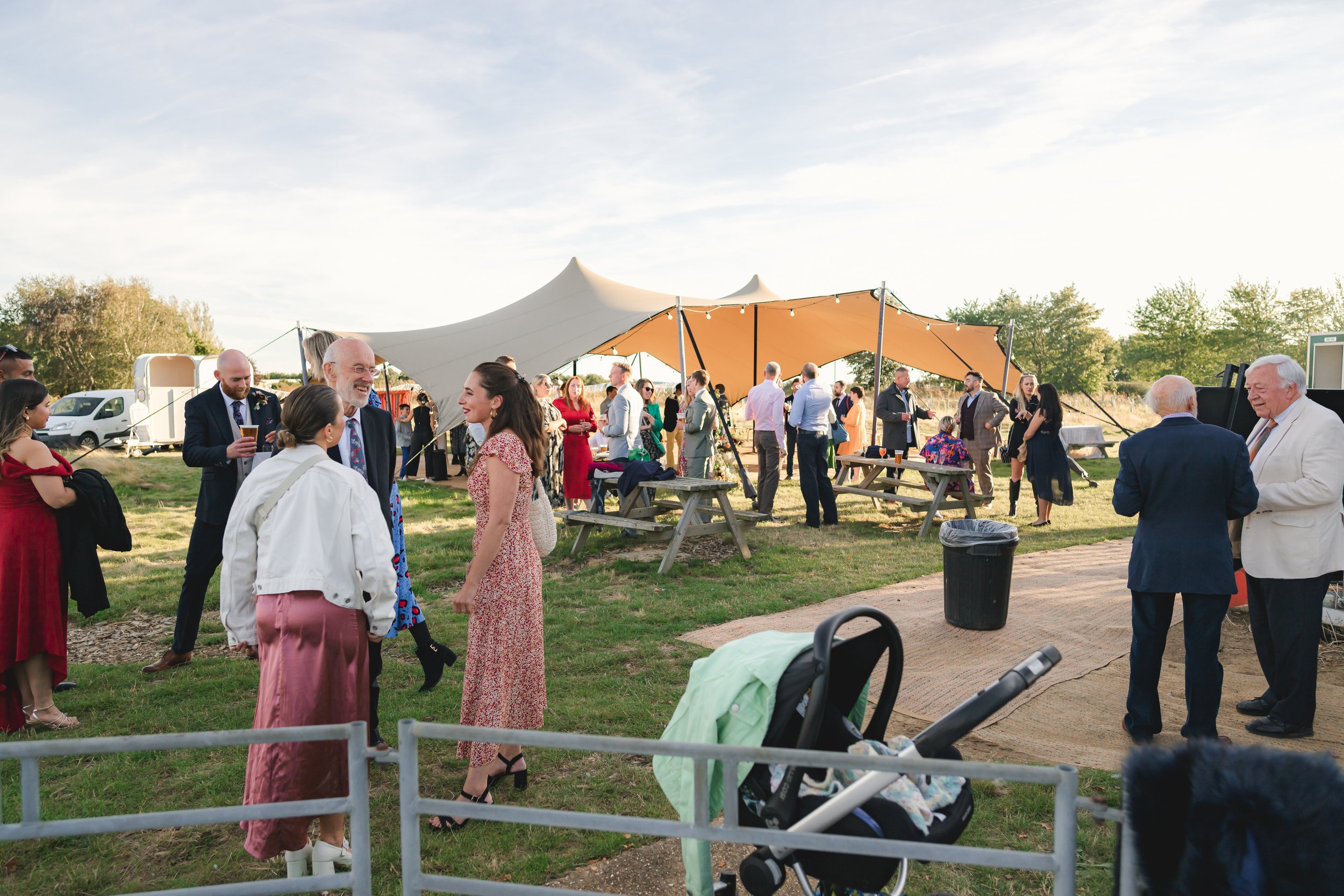 People socializing outdoors at a celebration or gathering with a large white tent in the background.