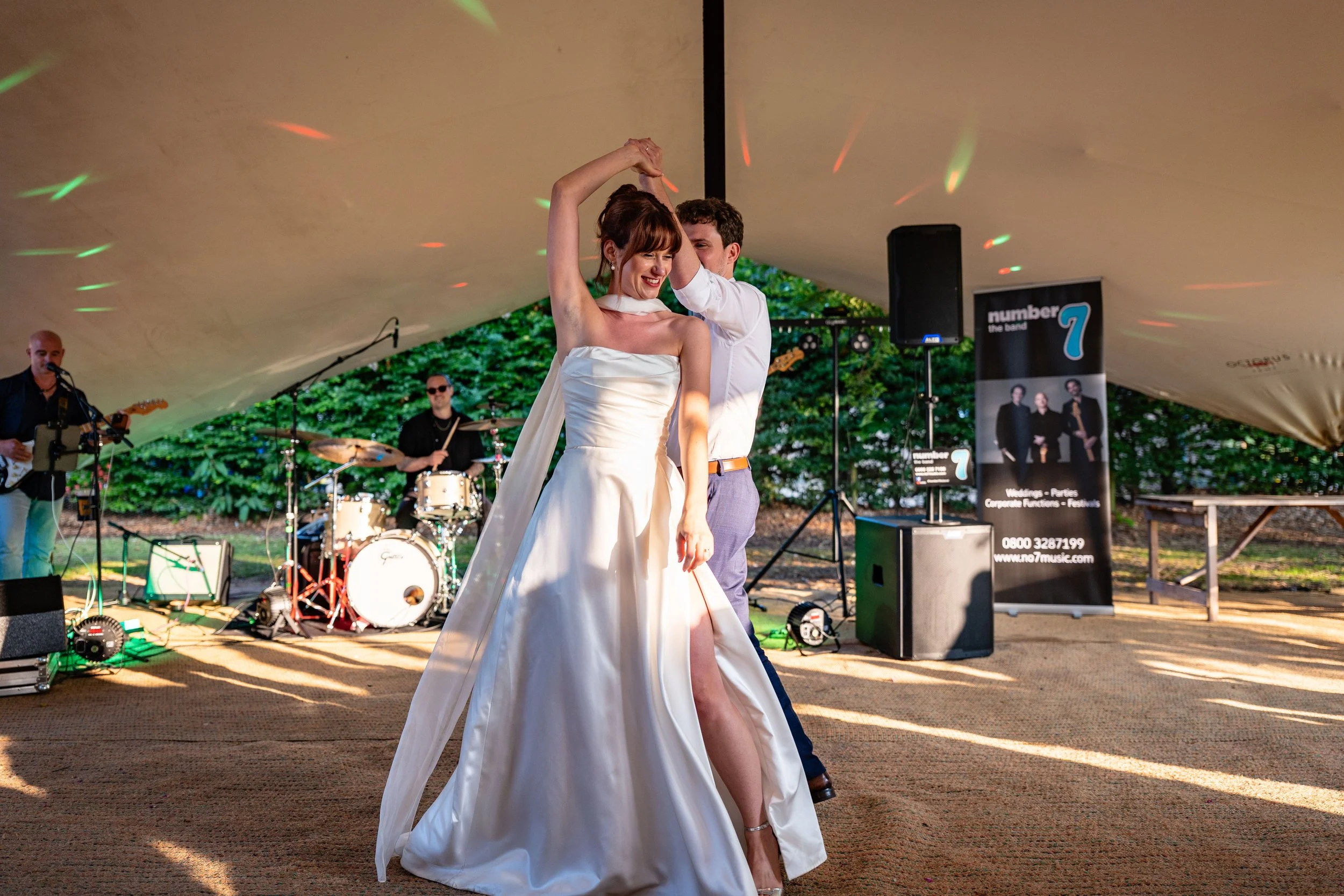 A bride and groom dancing under a tent during their wedding reception with a live band playing in the background.