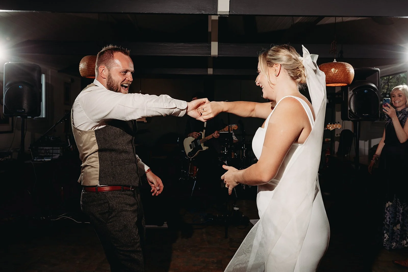 A bride and groom dancing and smiling together at their wedding reception, with a band playing in the background.