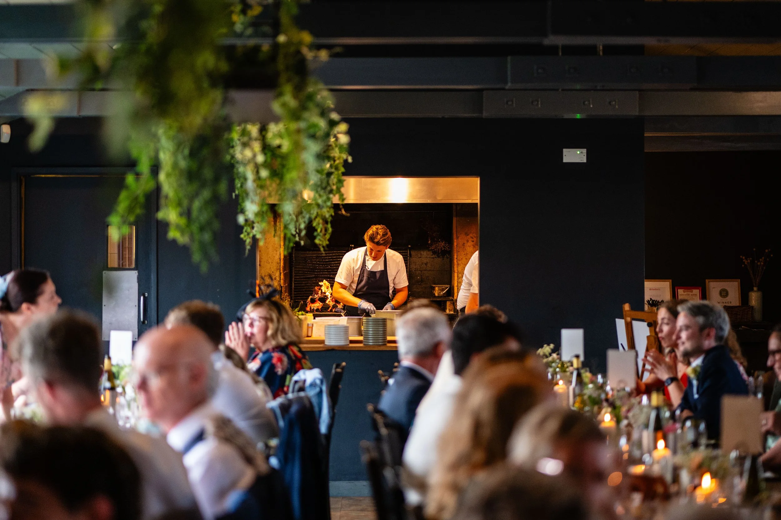 Chef cooking at an open kitchen in a restaurant filled with diners.