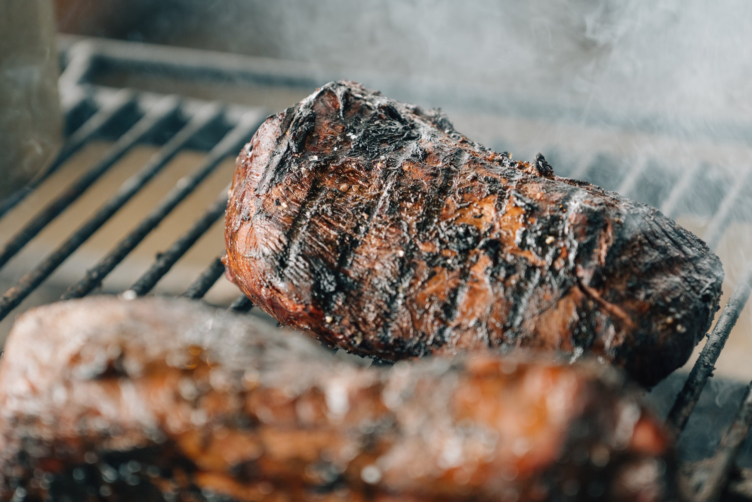 Two large pieces of grilled or smoked meat, possibly brisket, on a barbecue grill with visible char marks