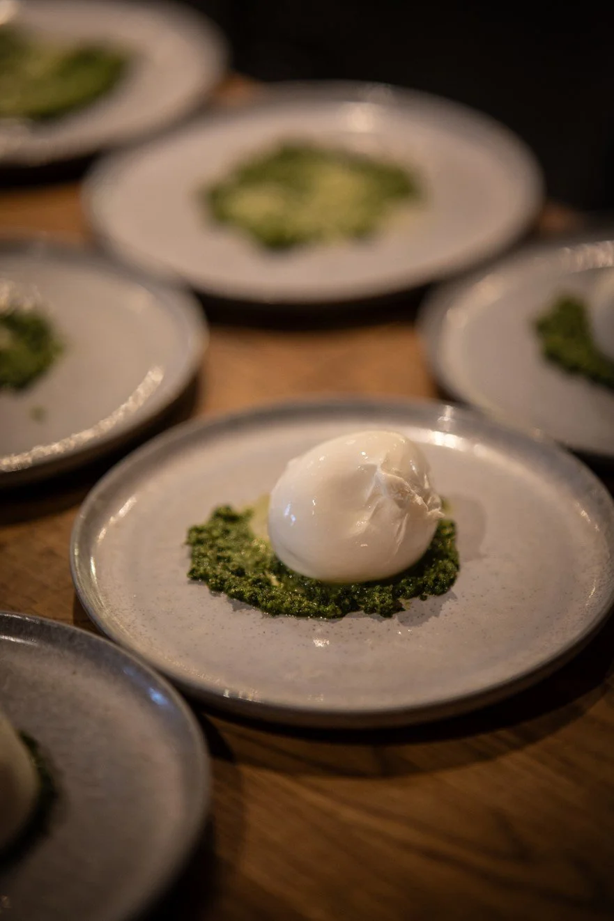 Small plate with a ball of mozzarella cheese on a bed of pesto sauce, surrounded by other similar plates.