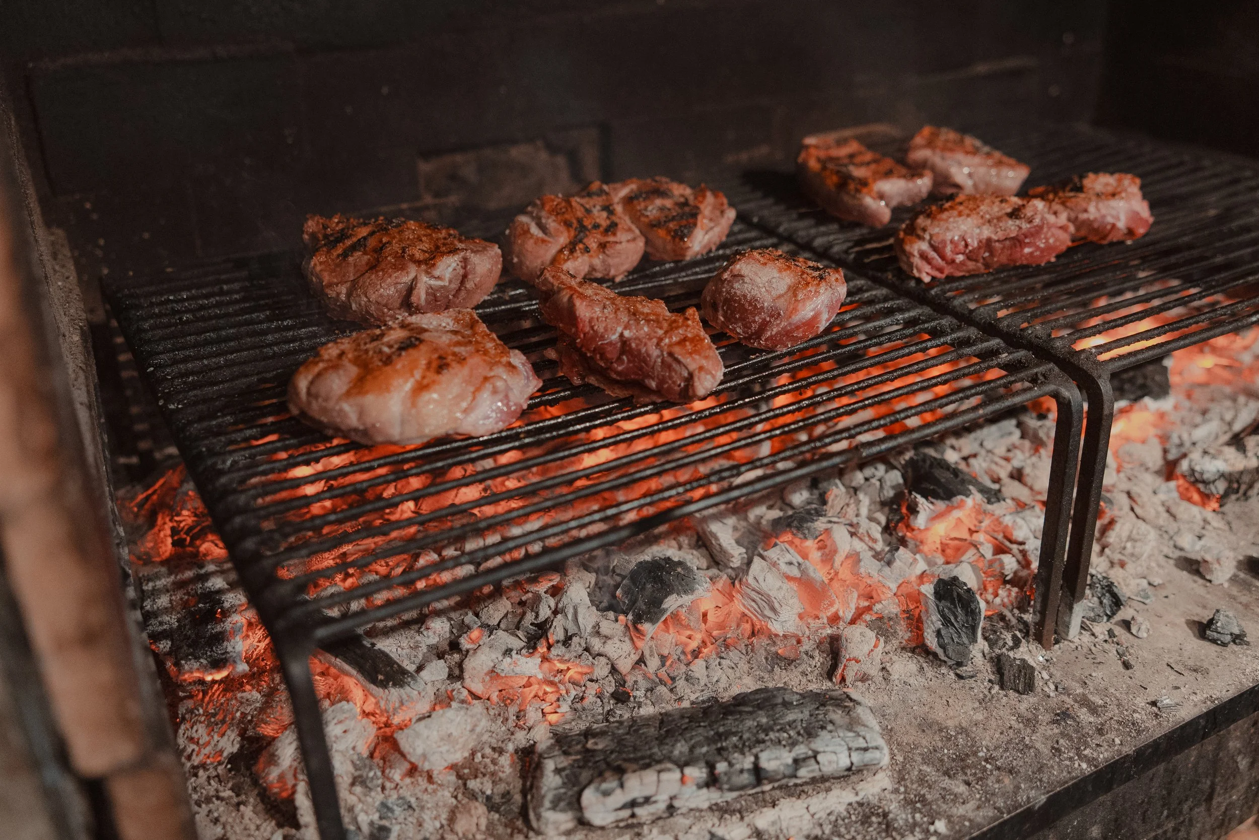 Meat sizzling on a grill over hot coals in an outdoor barbecue.