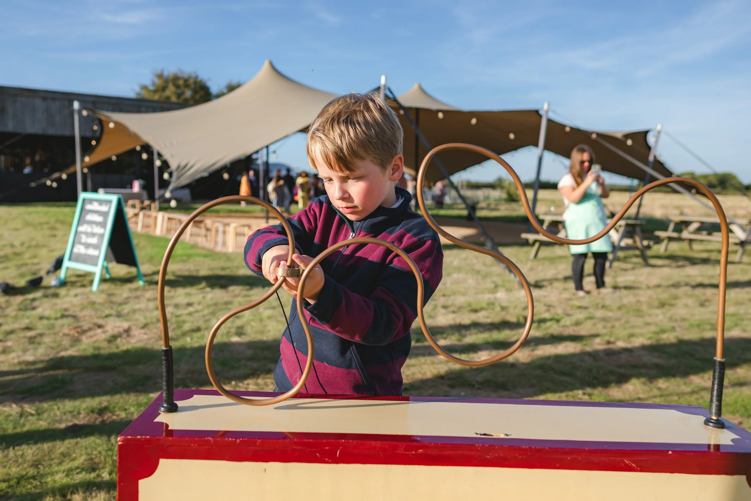 A young boy playing a loop-the-loop game at an outdoor fair or festival on a sunny day.