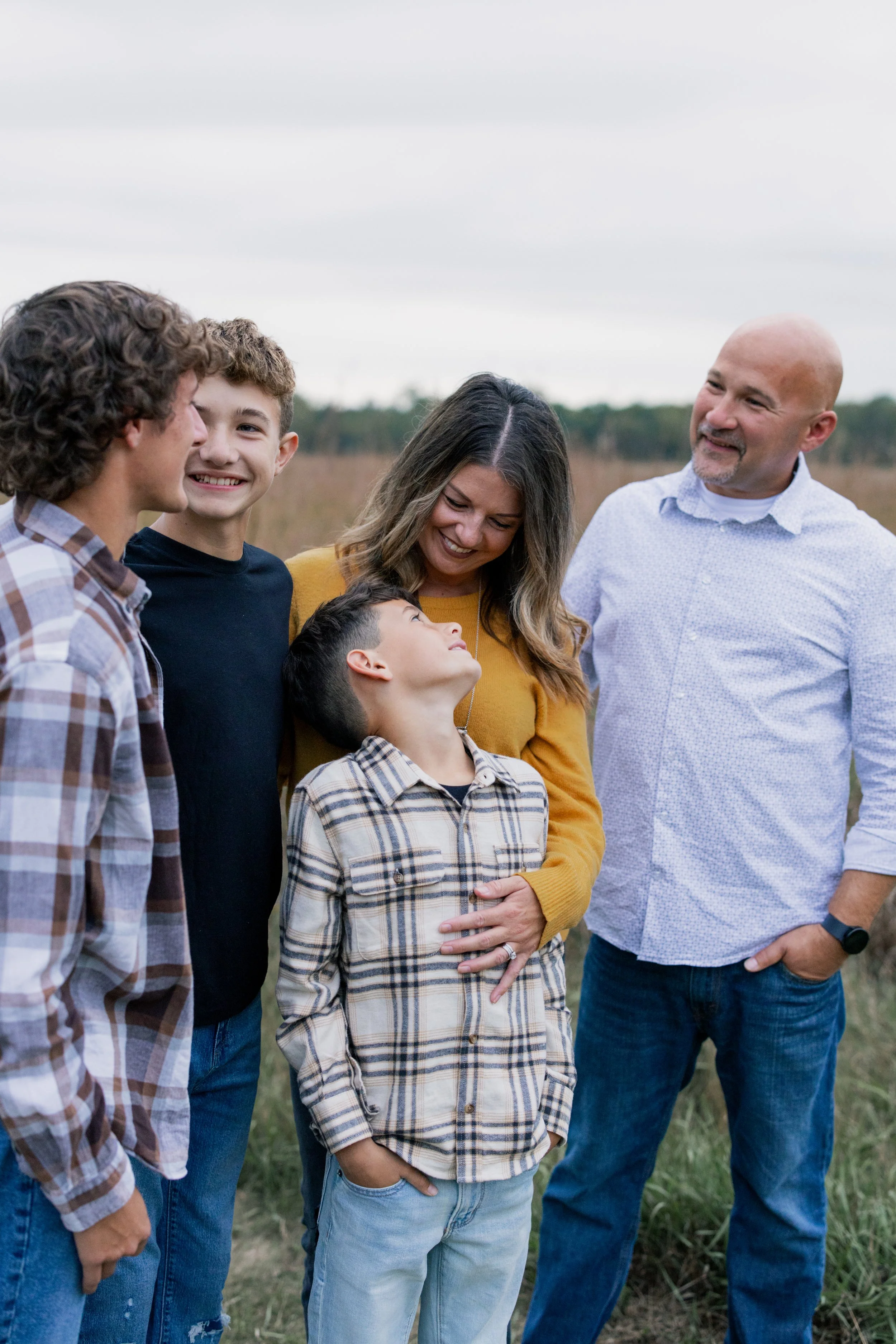 Family of five standing outdoors in a field, smiling and enjoying each other's company.