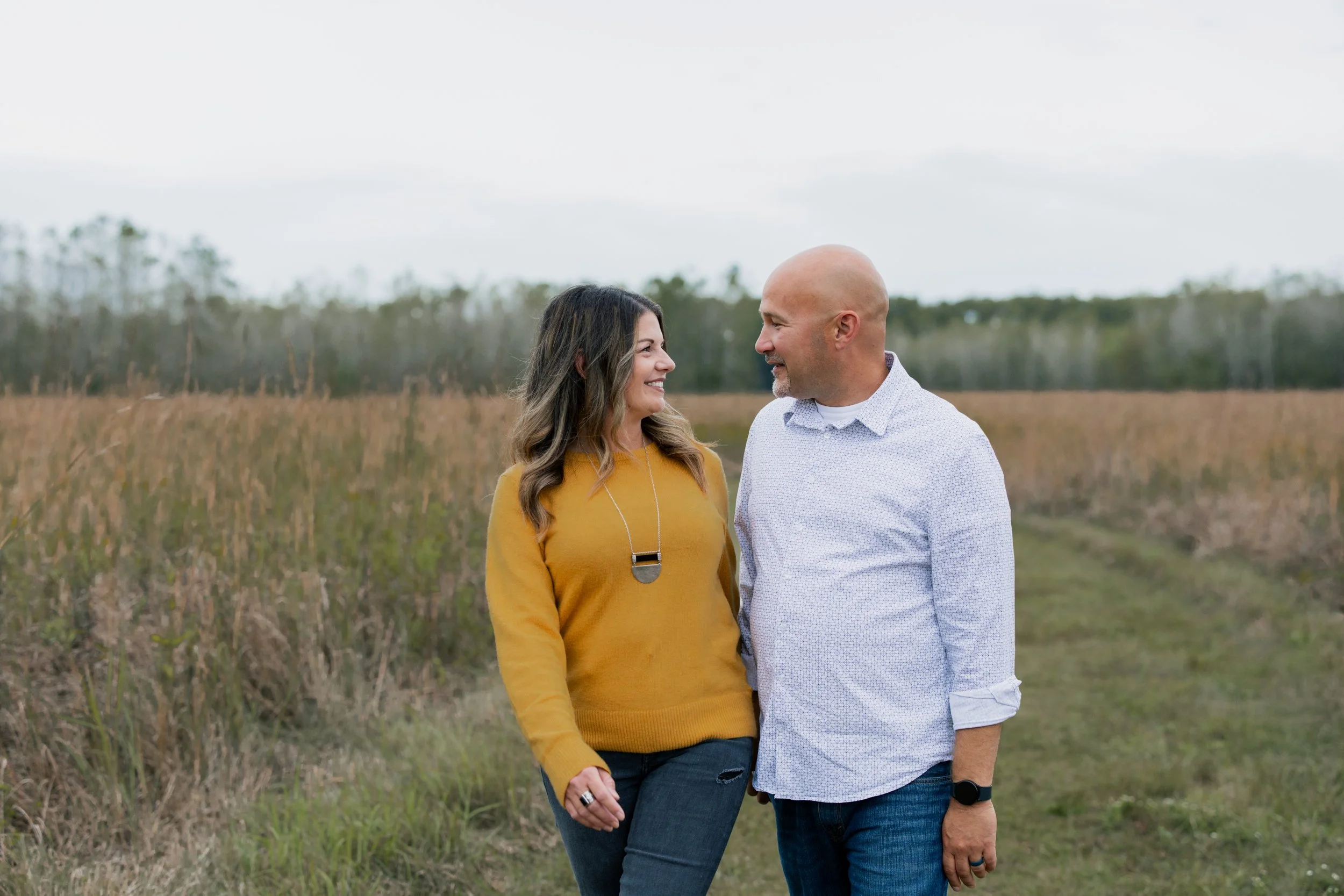 A man and woman smiling at each other outdoors in a field with tall grass or crops.