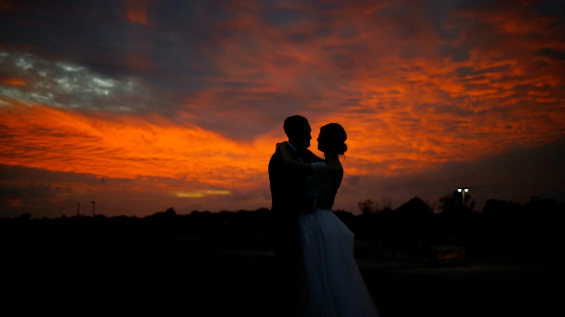 Silhouette of a couple embracing during a sunset with orange and purple clouds in the sky.