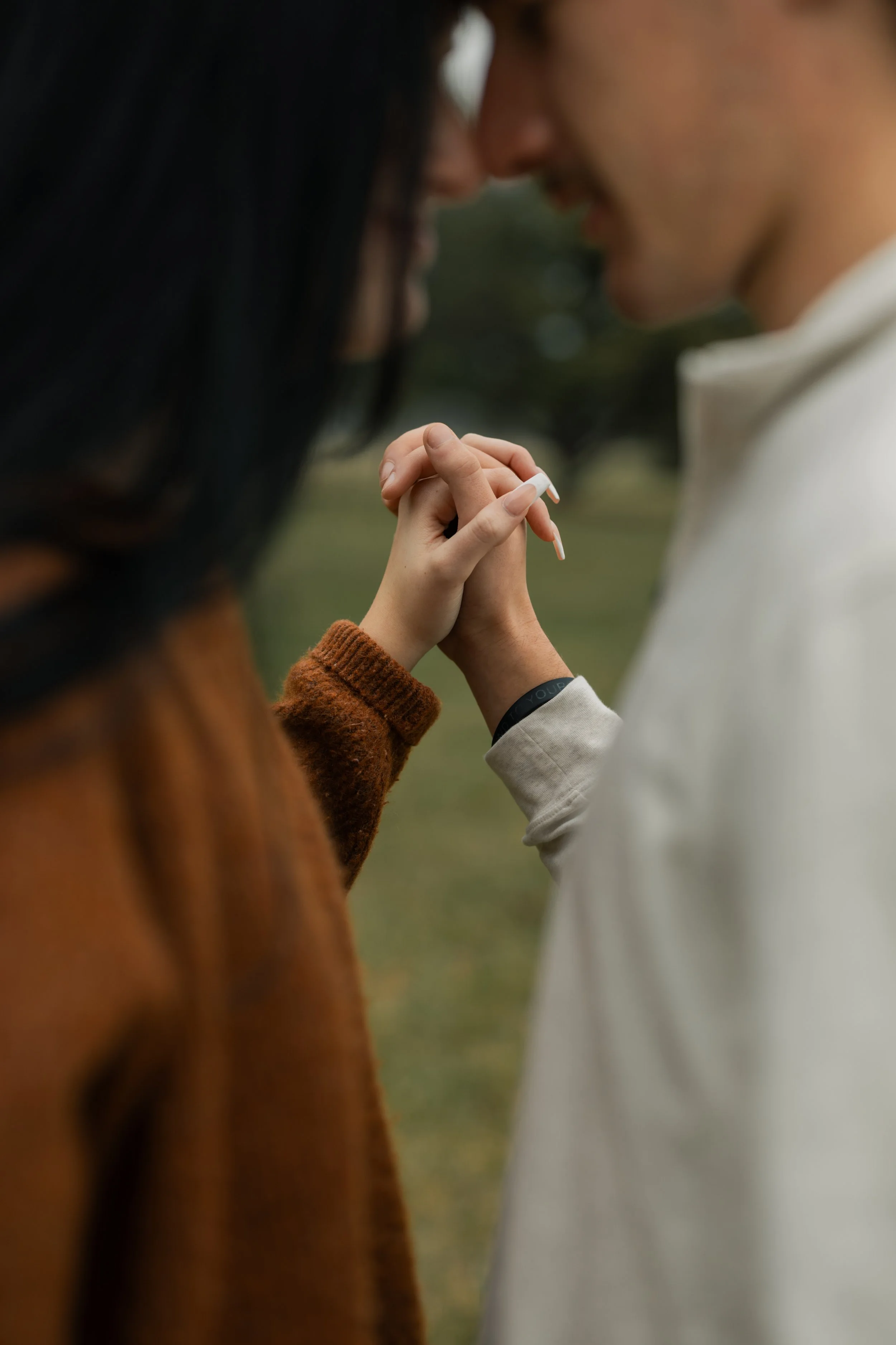 A close-up of a couple holding hands and touching foreheads outdoors, with blurred background.