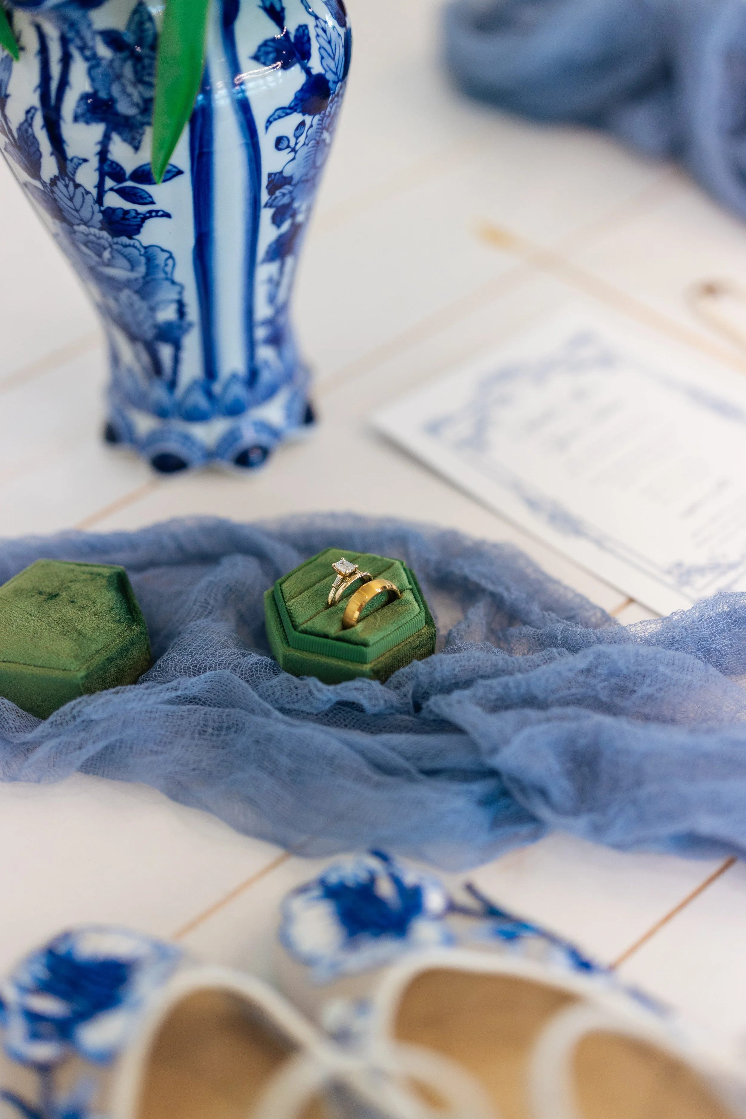 A jewelry display with gold rings, a blue and white vase, and glasses on a table.