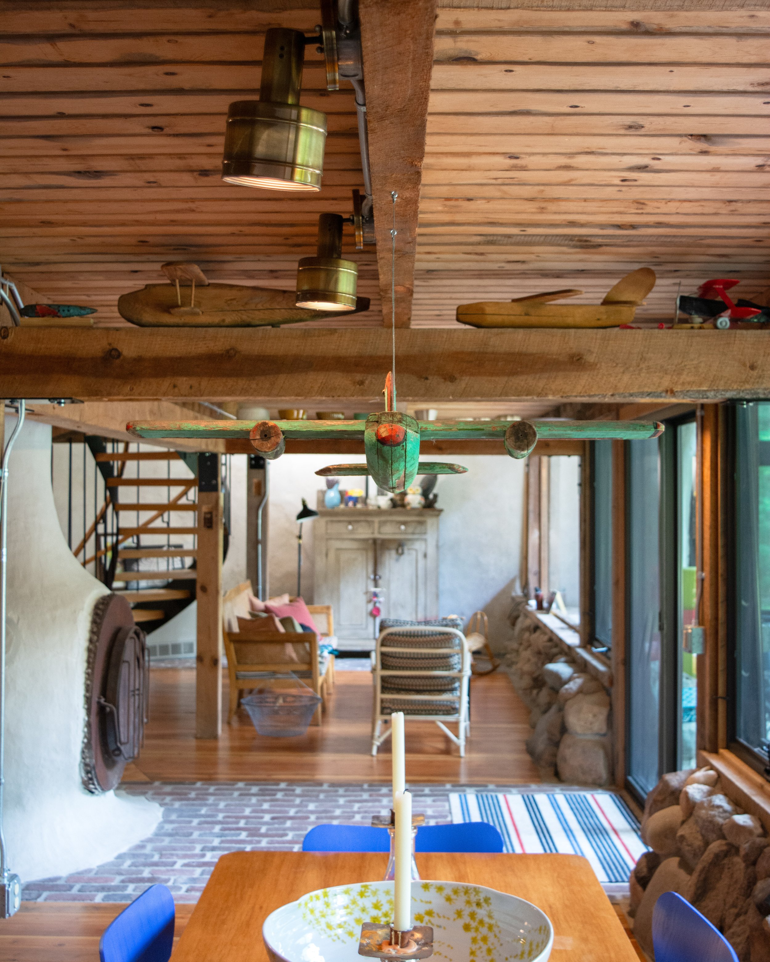 Indoor room with wood ceiling and walls, a wooden dining table with a candle, and a ceiling decorated with hanging wooden boats and a vintage airplane.