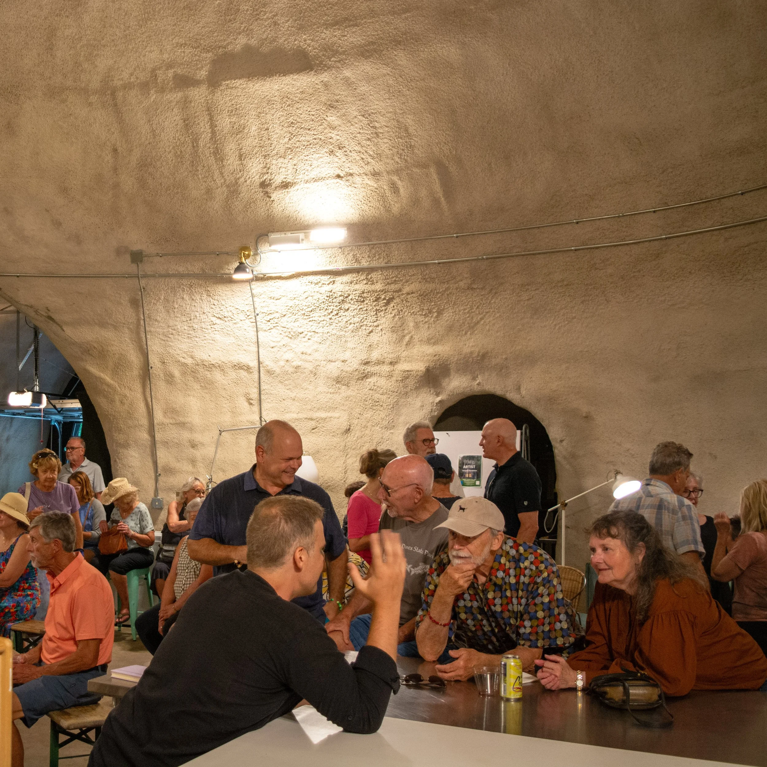 People socializing and chatting in an underground venue with rough textured walls and overhead lighting.