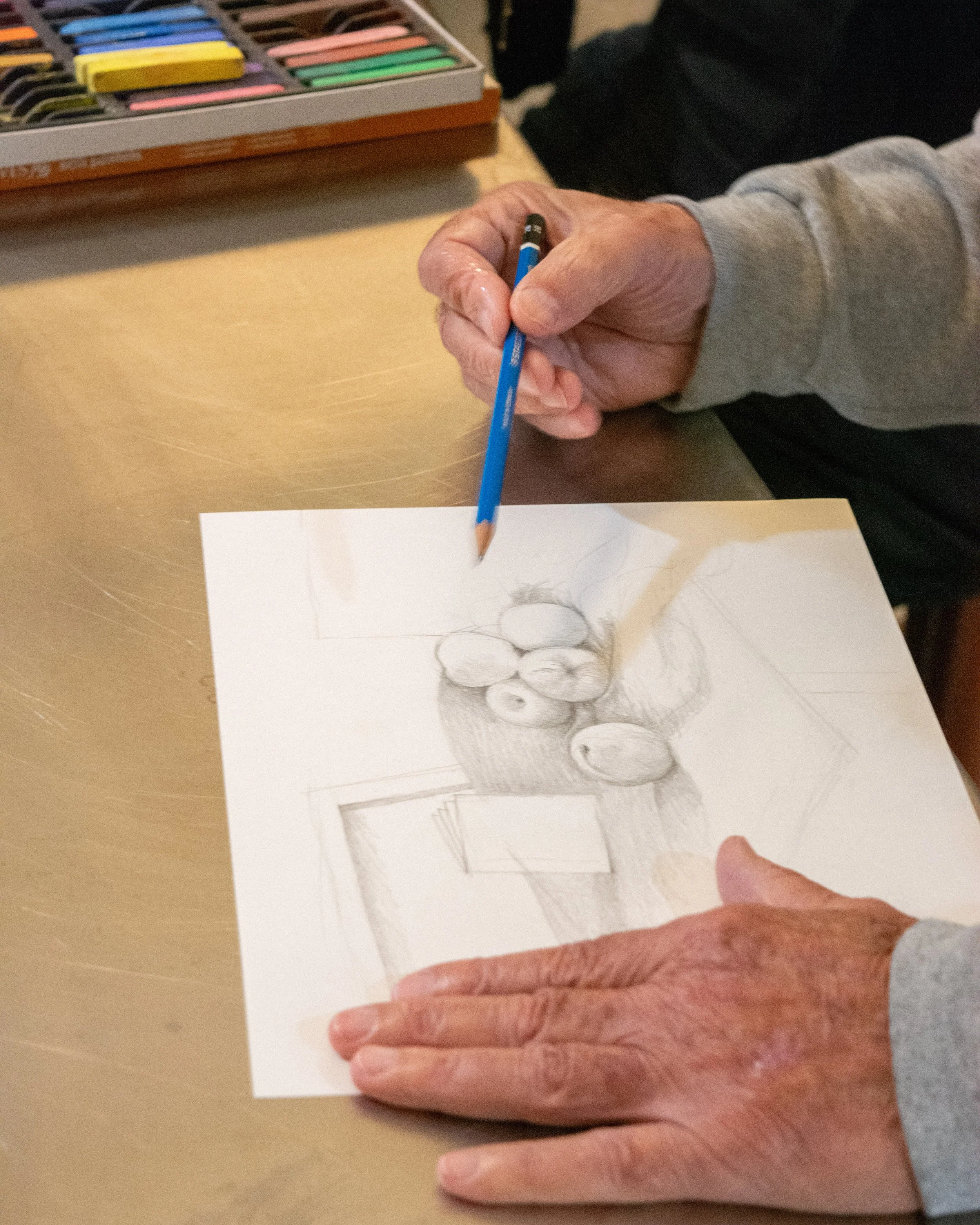 Sketching a still life drawing of eggs on paper, with pastels in a box on a wooden table at the Dome House