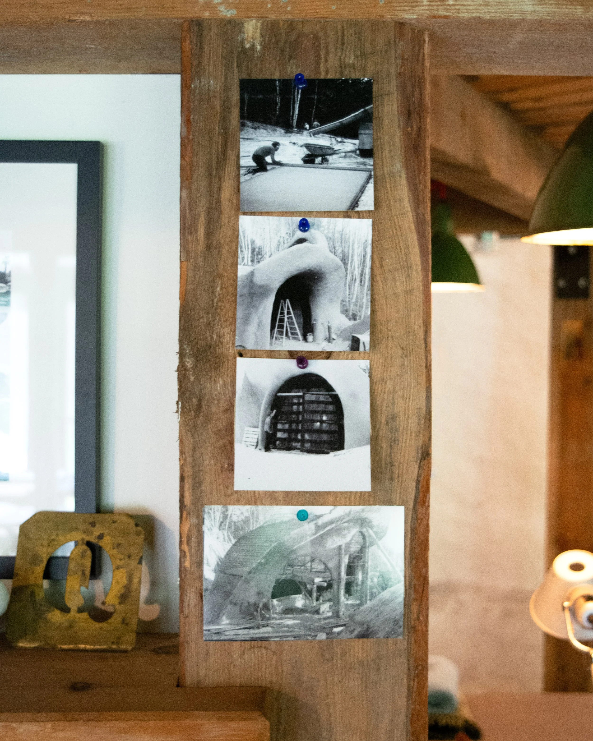 Four black-and-white photographs pinned on a wooden board, depicting construction or excavation scenes with structures resembling domed buildings.