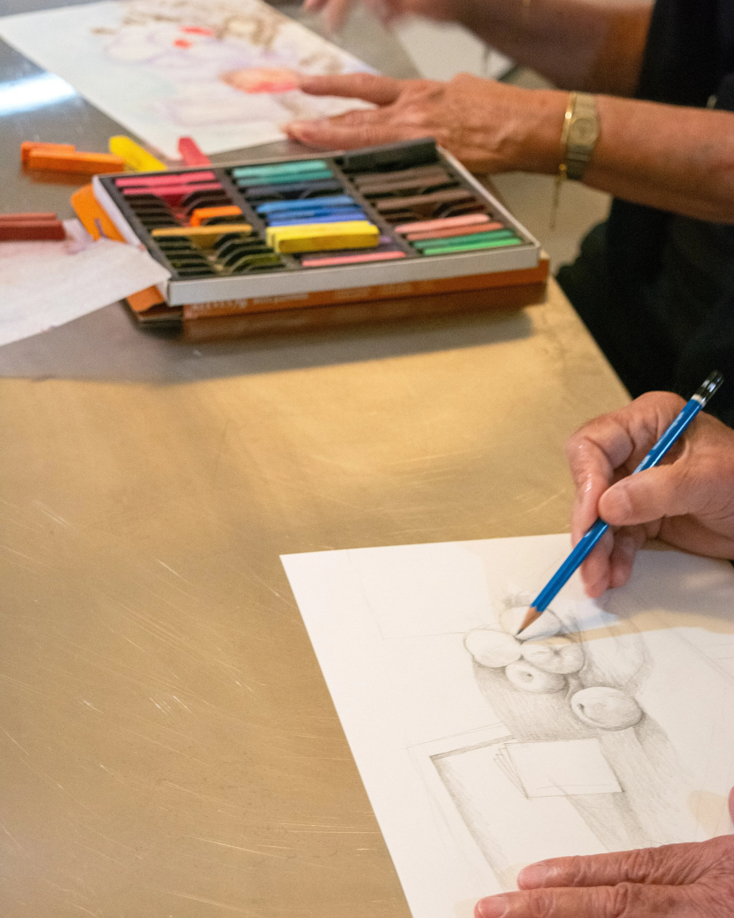 Person drawing a still life of pears on paper with colored chalks nearby.