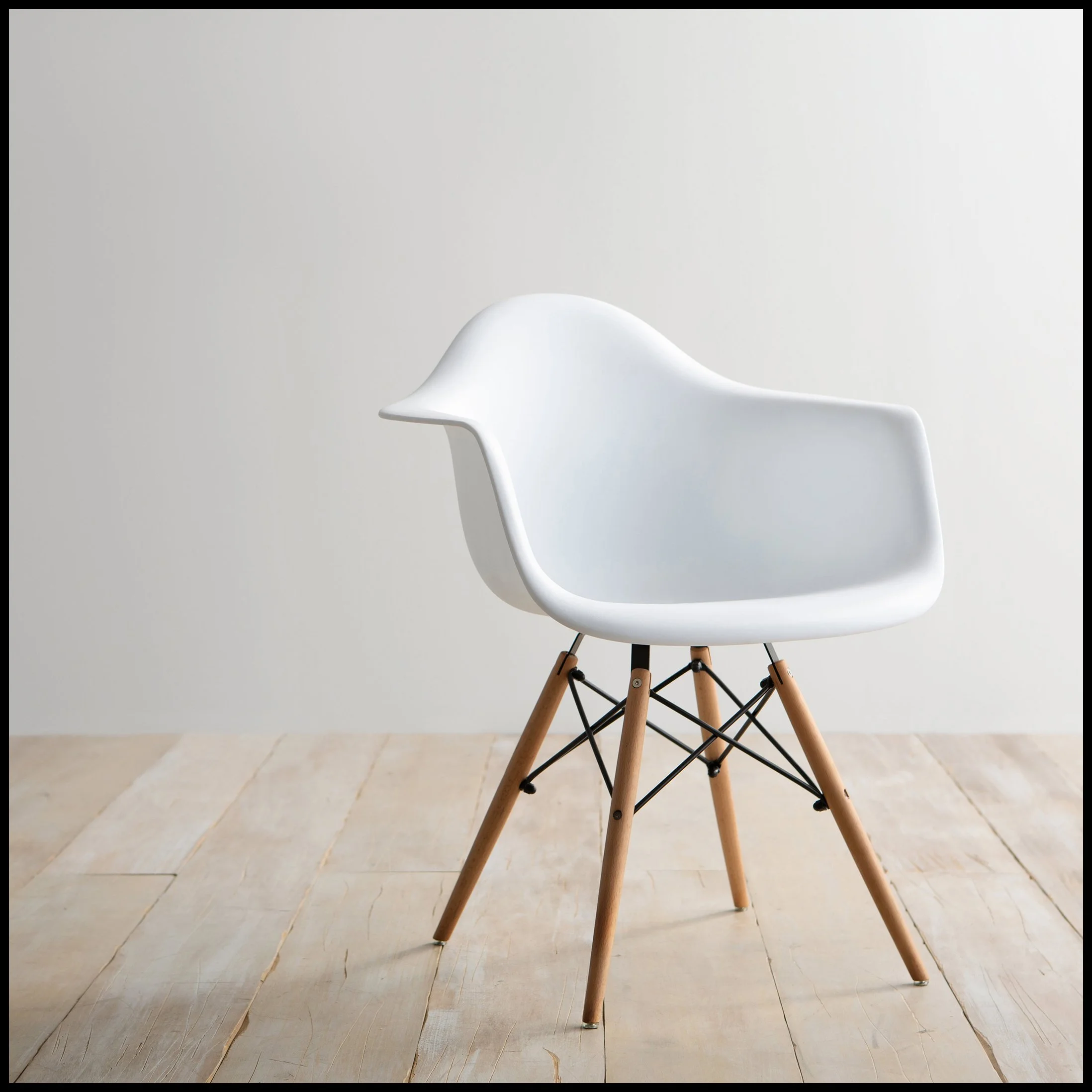 Modern white chair with wooden legs and black metal supports on a light wooden floor against a plain white wall.