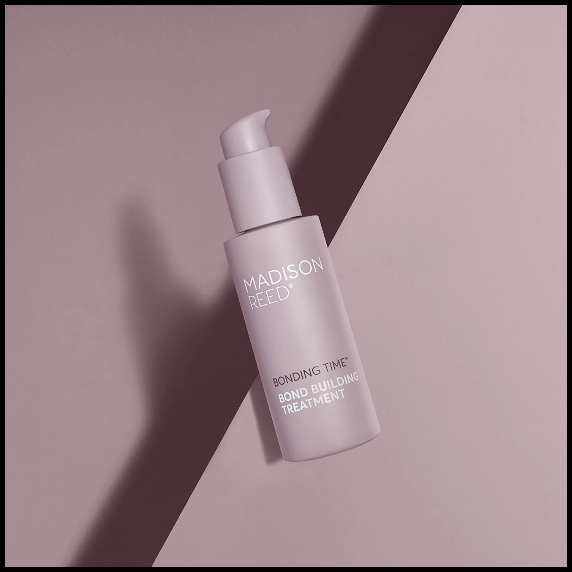 A bottle of Madison Reed Bonding Time Bond Building Treatment with a pump dispenser, placed on a pink background with a diagonal shadow.