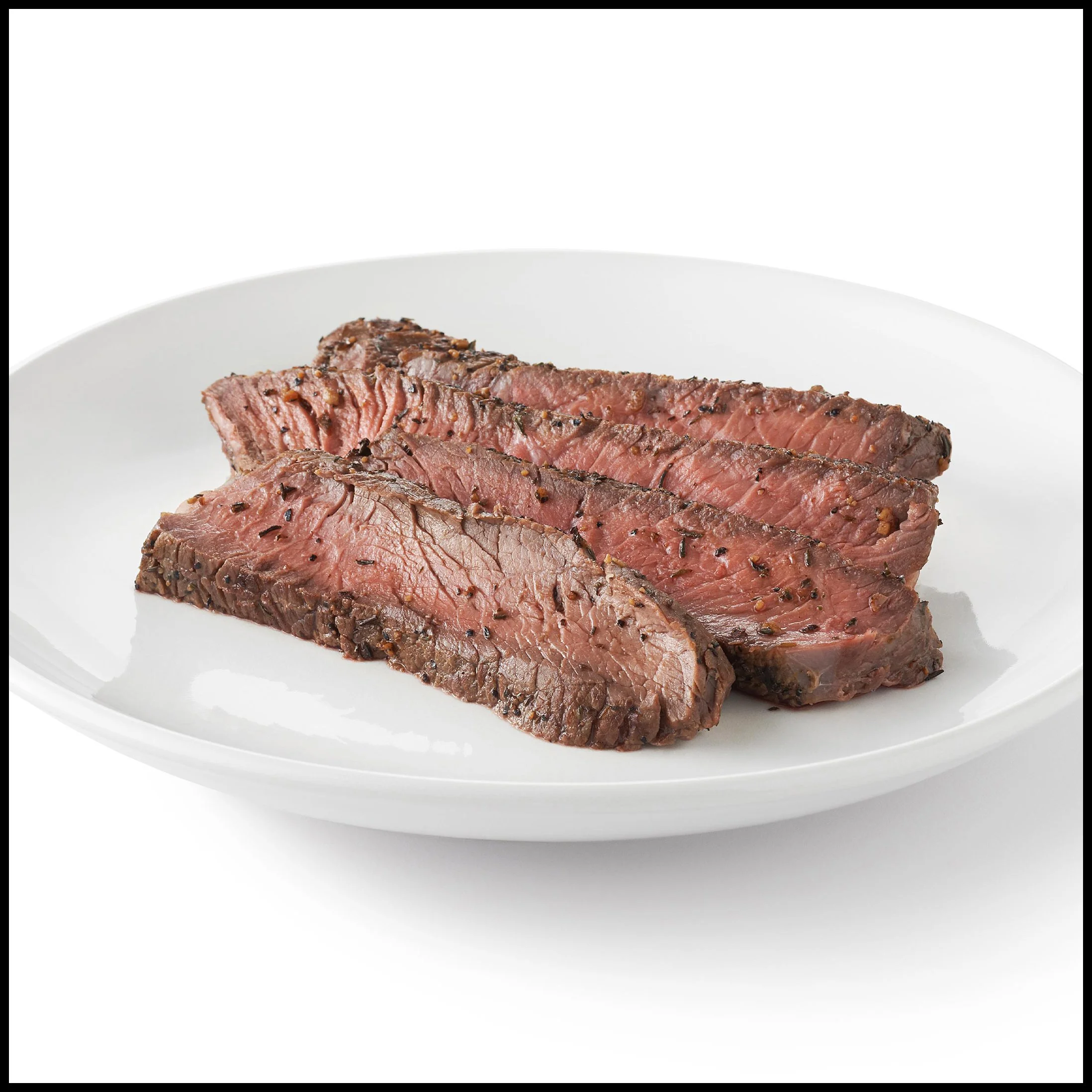 Sliced medium-rare steak garnished with black pepper on a white plate.