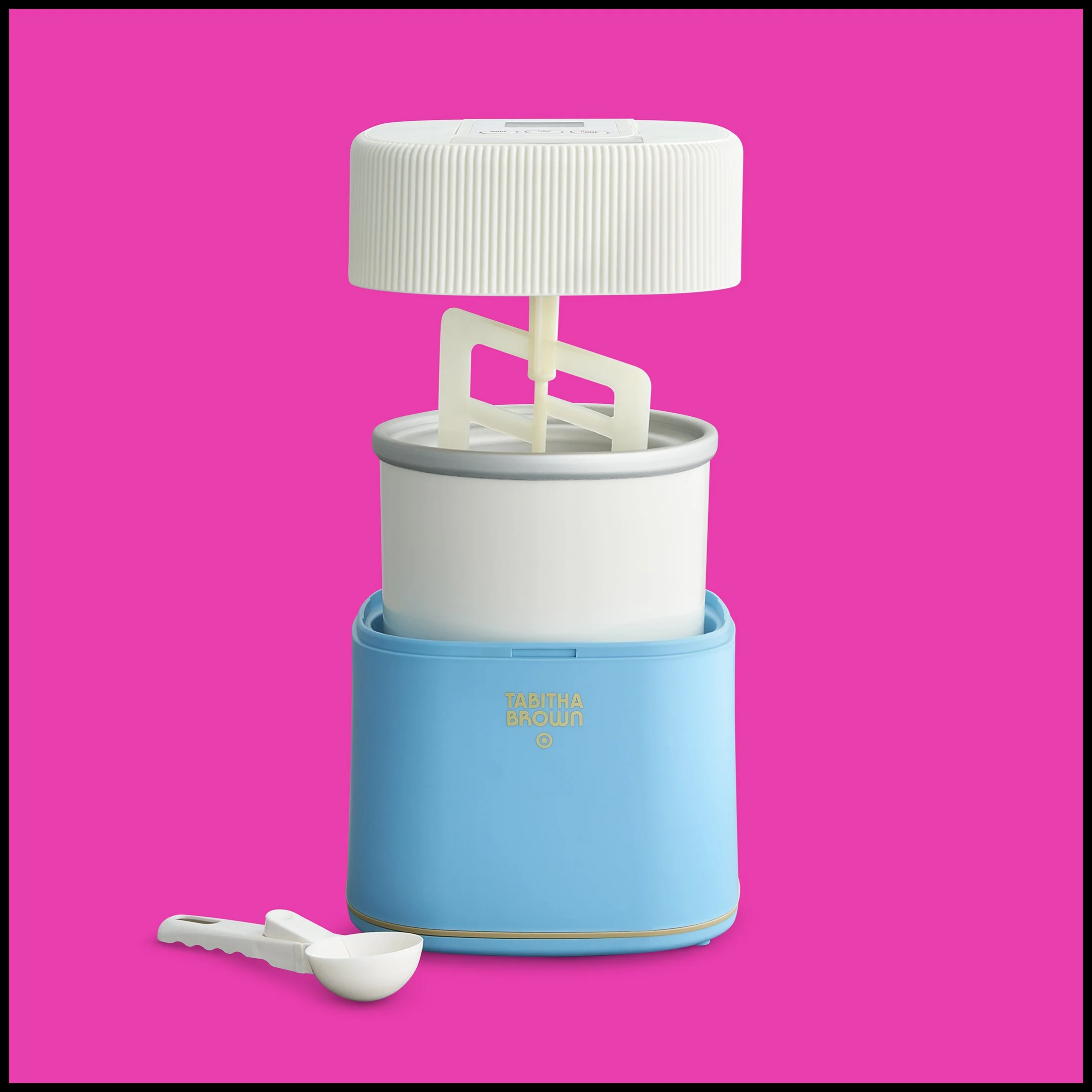 A vintage-style ice cream maker with a blue base, a white inner bowl, and a white lid, against a pink background, with a white scooper in front.  Target Tabitha Brown Ice Cream Maker Product Advertising Photography KyleSmithPhoto.