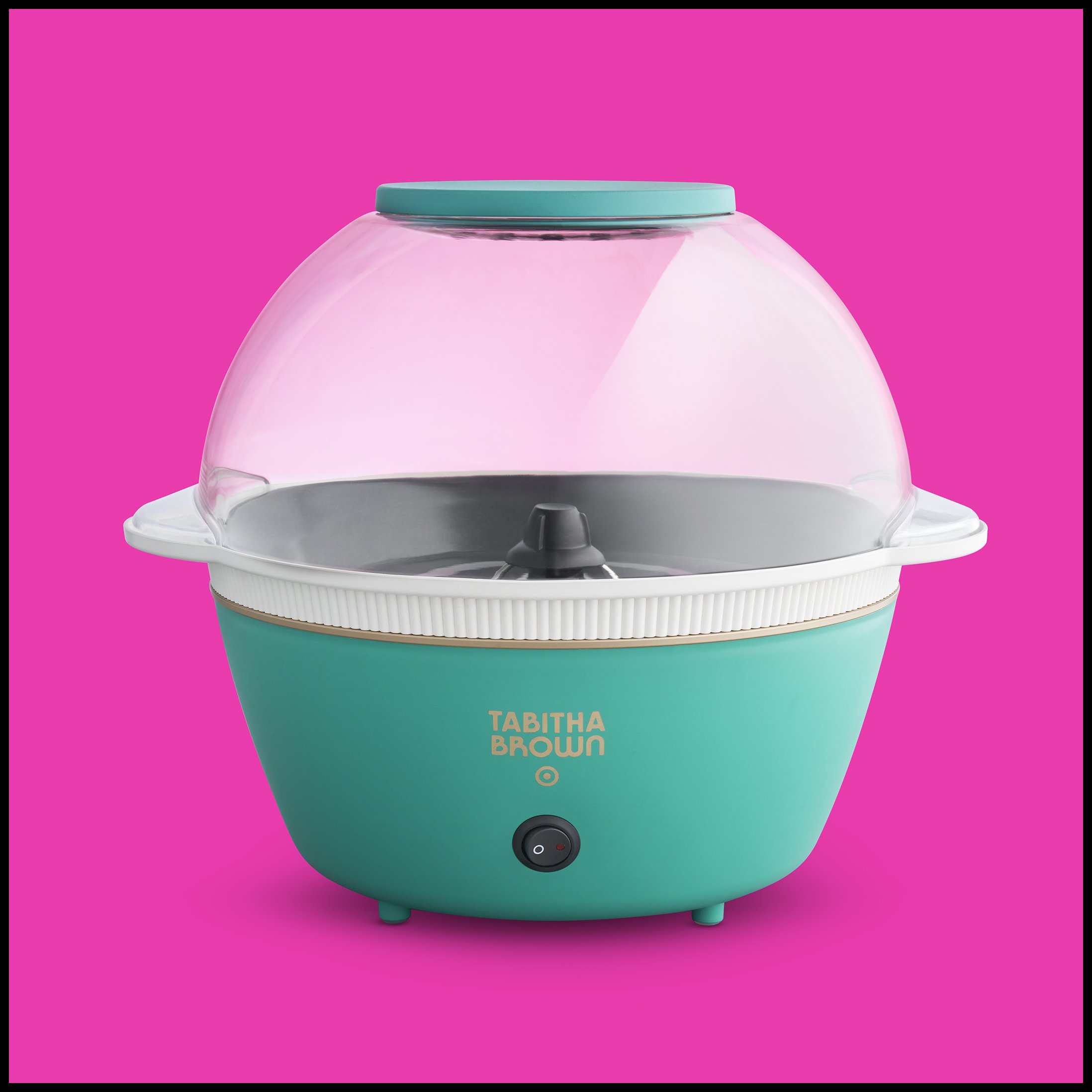 A vintage-style teal and white popcorn machine with a clear plastic dome, set against a bright pink background.  Target Tabitha Brown Popcorn Maker Product Advertising Photography KyleSmithPhoto.