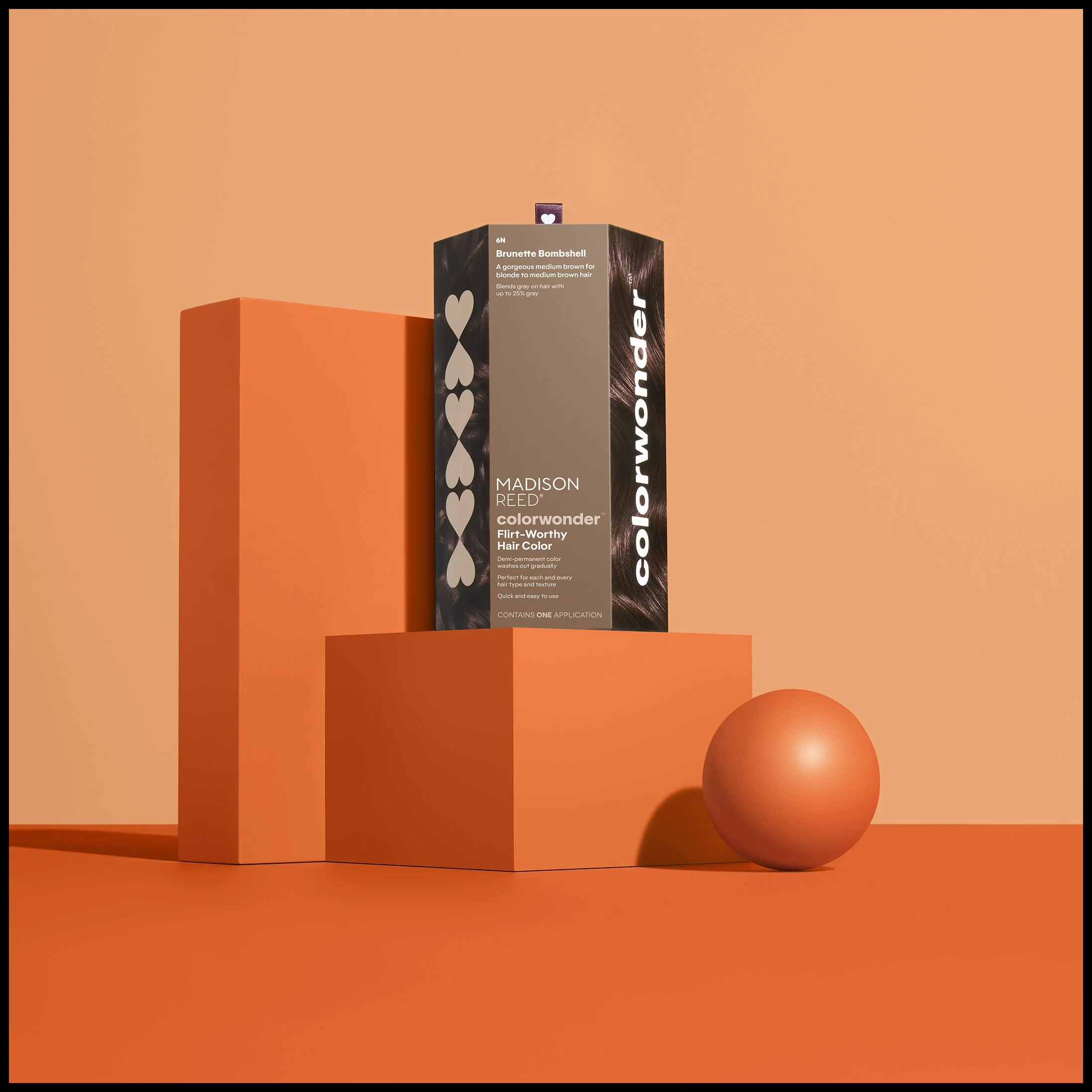 A box of Madison Reed ColorWonder hair dye standing on a small orange platform with a peach-colored background. Next to it is a peach-colored sphere.