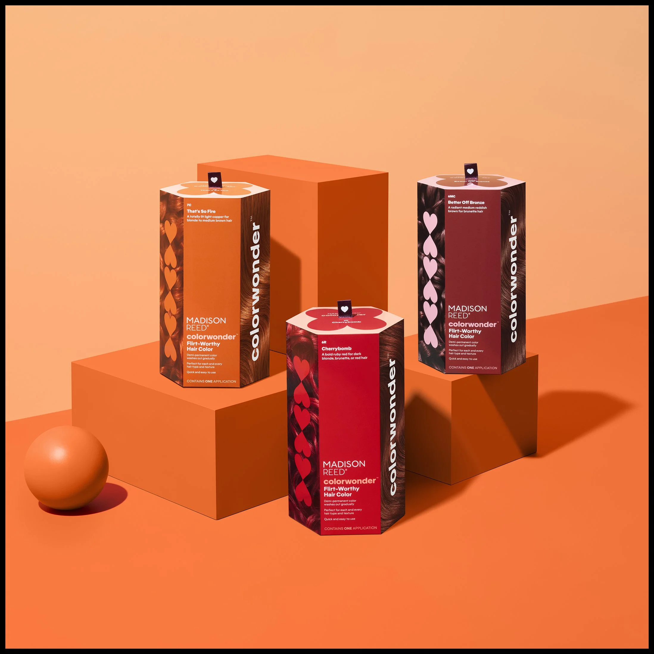 Three boxes of Madison Reed ColorWonder hair dye in red and purple shades, displayed on orange platforms with a peach-colored background.