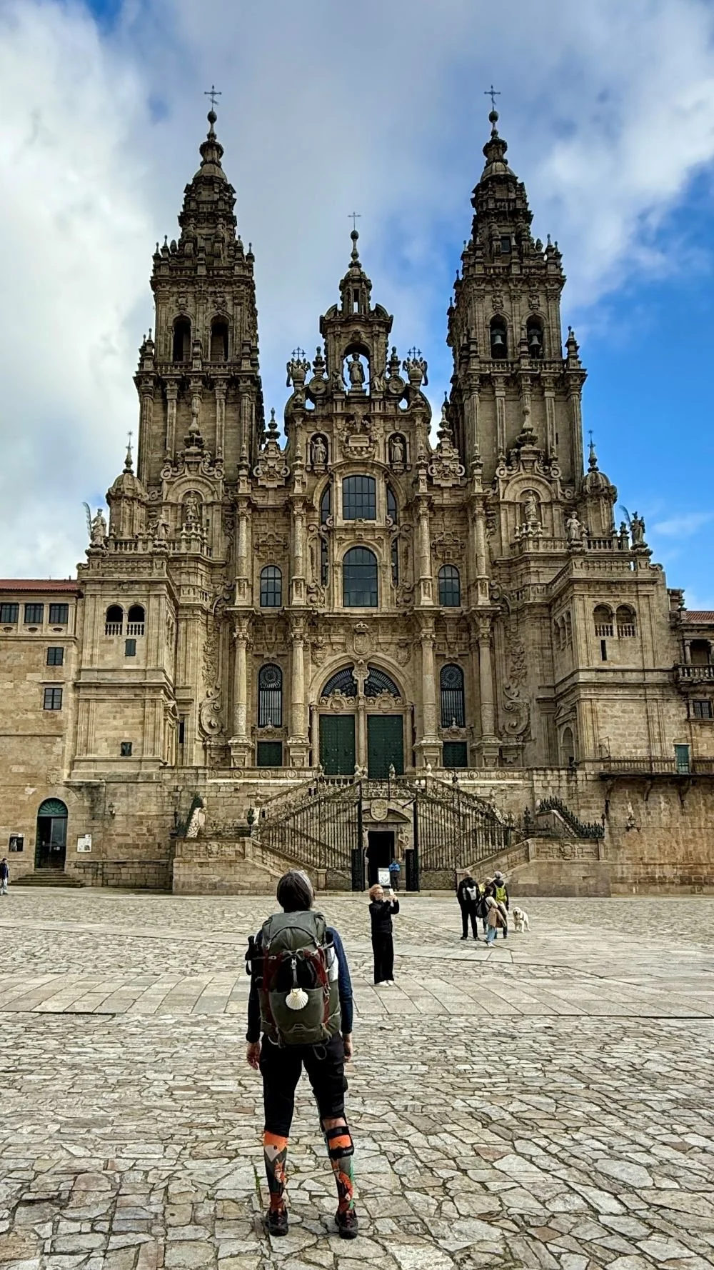 a solo woman pilgrim stands at the cathedral in Santiago de Compostela after completing the Camino Portuguese