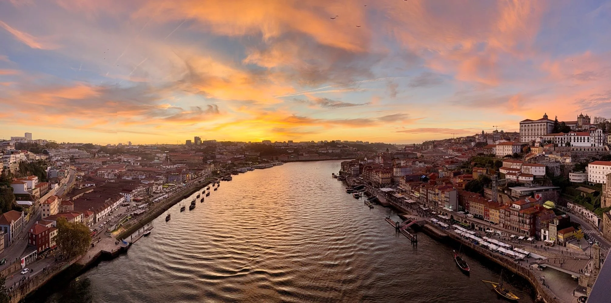 Sunset over the Douro River in Porto, Portugal, with city buildings glowing in warm evening light