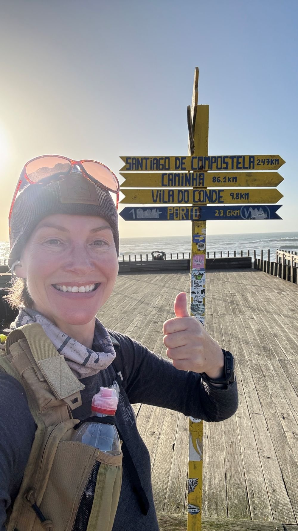 Emma Hull smiling and posing beside a signpost for Santiago de Compostela while walking solo along the coastal route of the Camino Portuguese