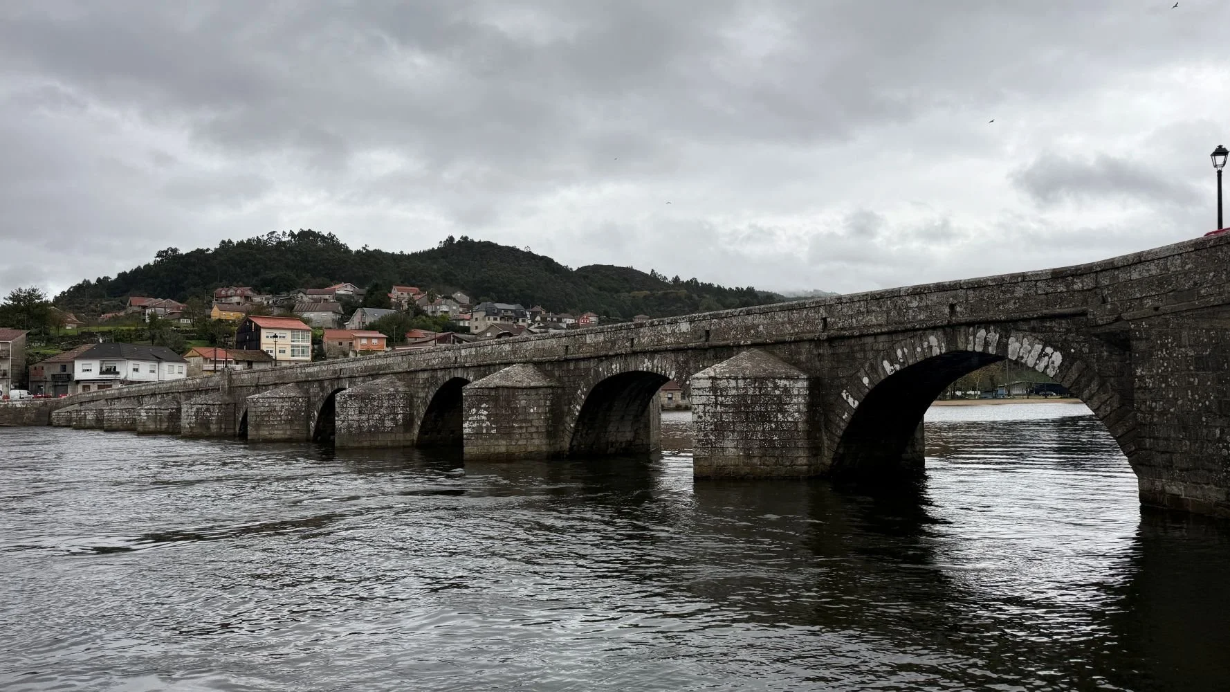 Historic stone bridge on the Camino de Santiago crossing a wide river under a cloudy sky