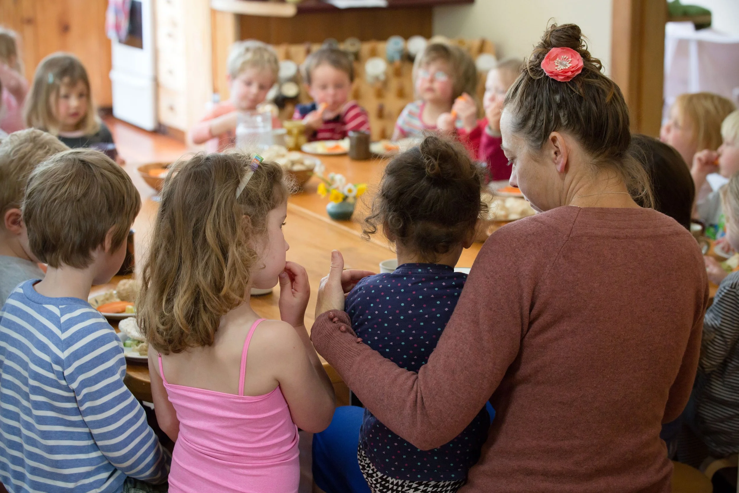 Young child sitting on a teachers knee at the lunch table