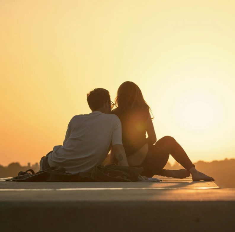couple sitting together on the ground watching the sunset
