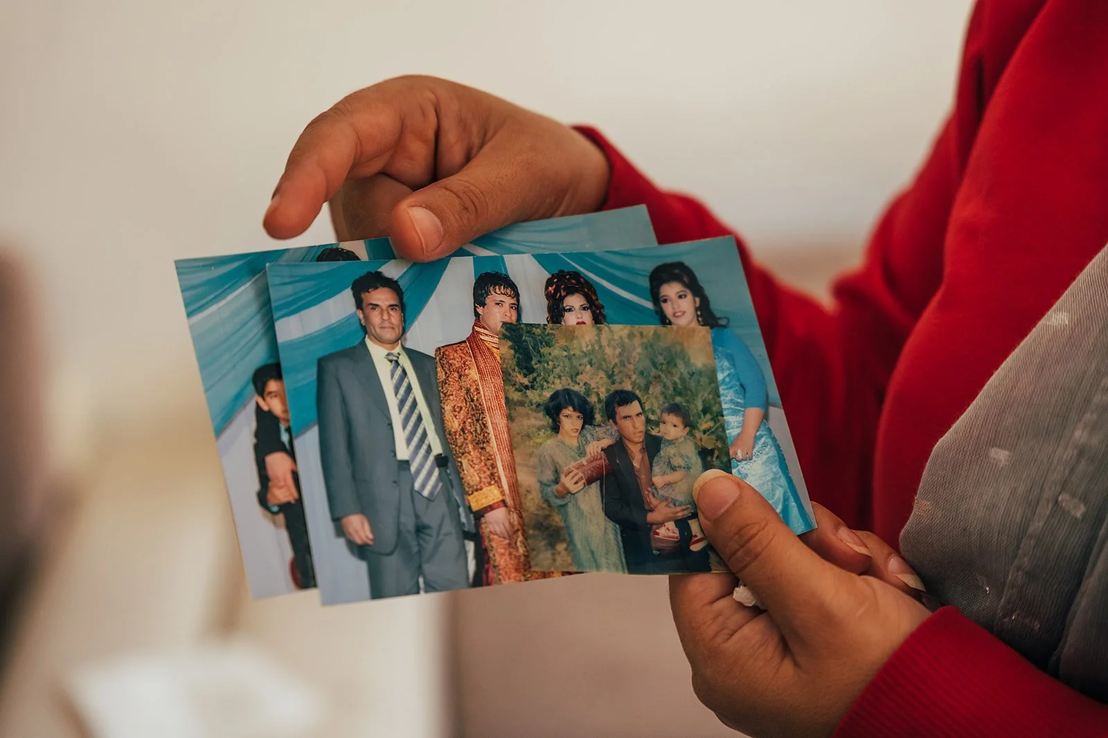 Person holding three photographs showing a group of people, some dressed in formal traditional attire, outdoors and at an event.