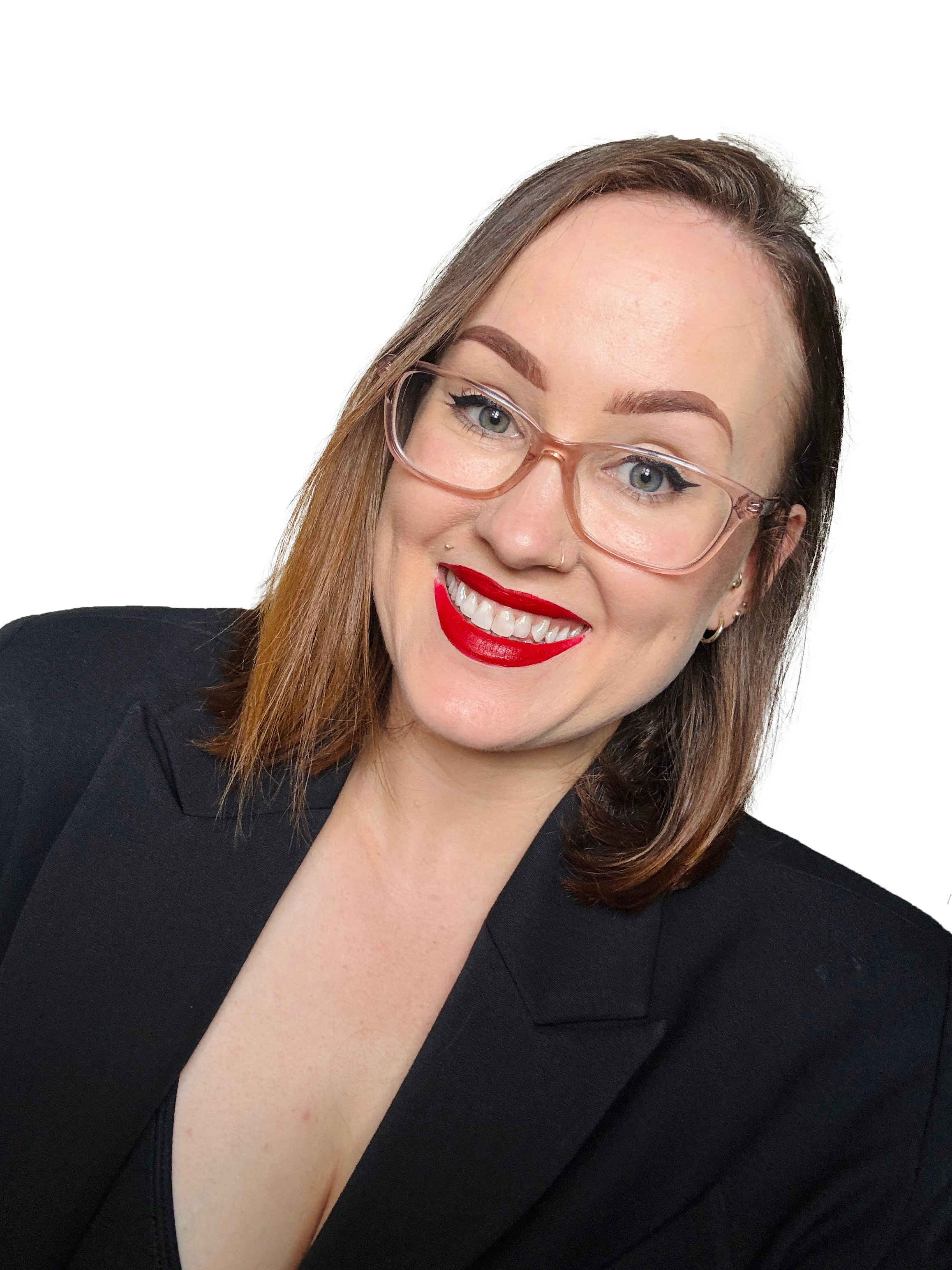 Close-up of a woman with light skin, wearing pink glasses, red lipstick, and a black blazer, smiling against a plain background.
