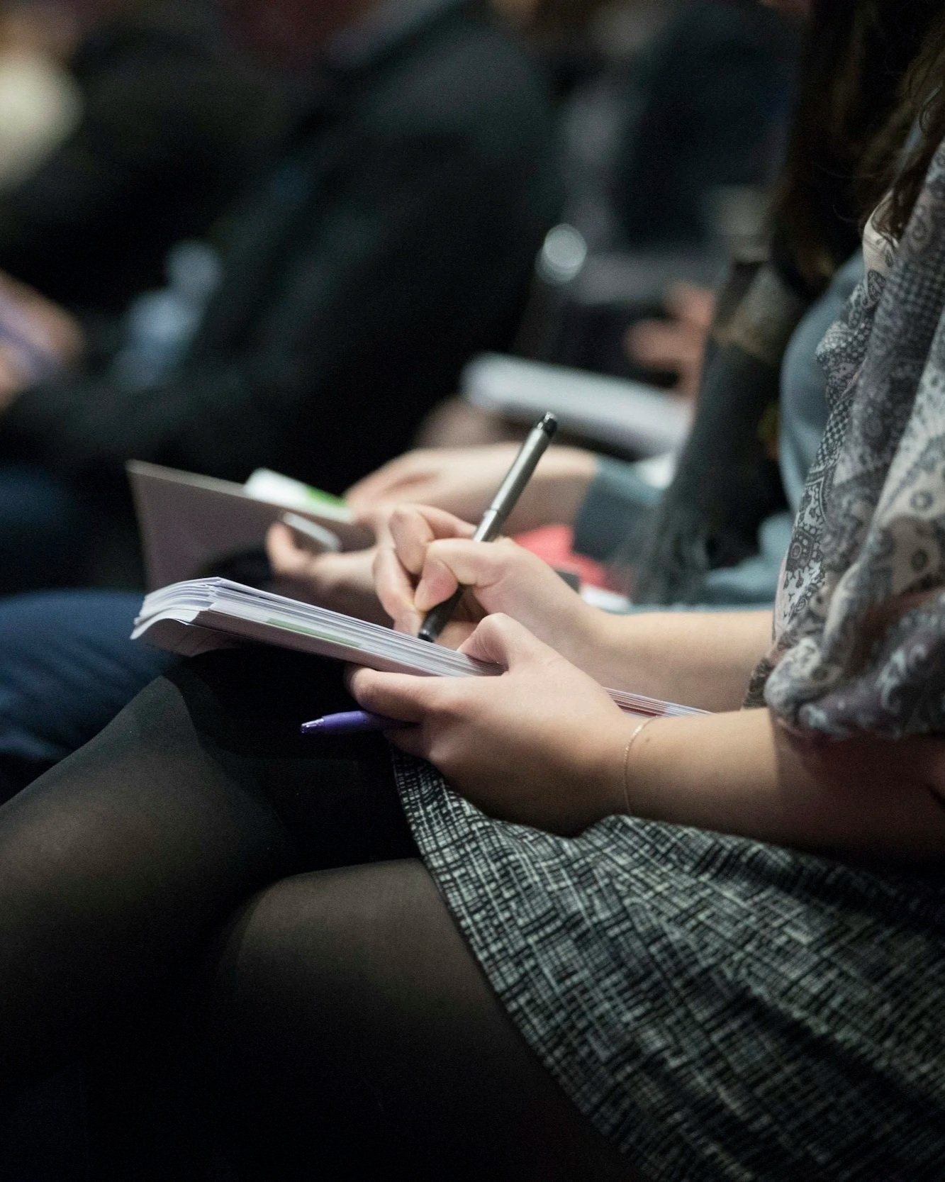 Close-up of a person's hands holding a notebook and writing with a pen in a dimly lit setting.