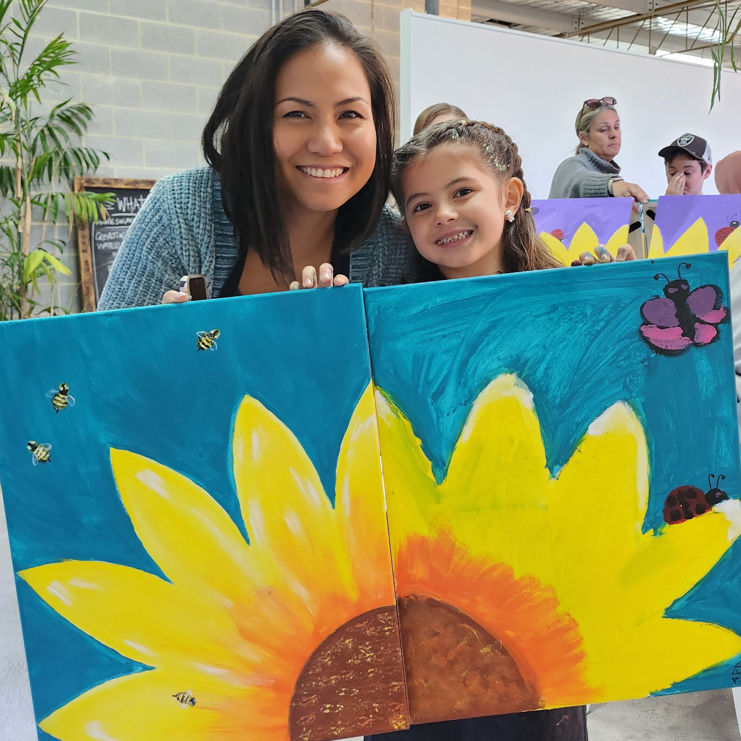 Mum and daughter attending Leigh Binskin Art's Adult and Child paint Date. Participants holding sunflower painting.