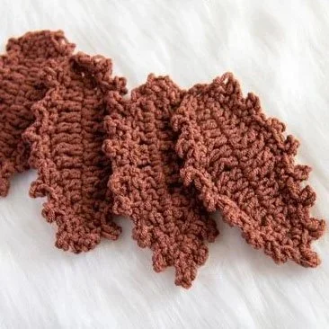 Four chestnut coloured, oval shaped leaves are laying on an off white surface. They are overlapped onto each other and each have a bobbly edge