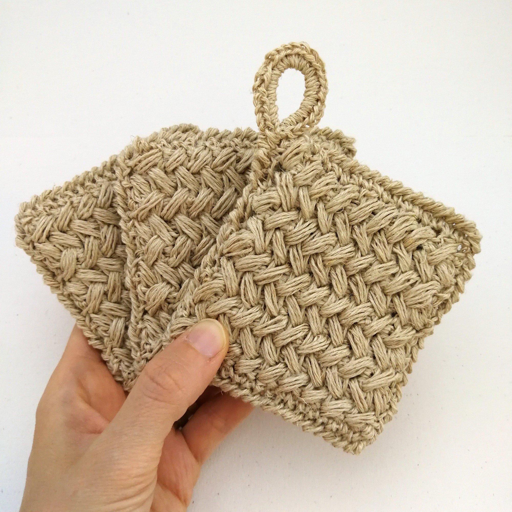 A left hand is holding 3 crochet kitchen scrubbies like a deck of cards. They have a braided type pattern. The sponge on the top has a small hanging loop on the top left.