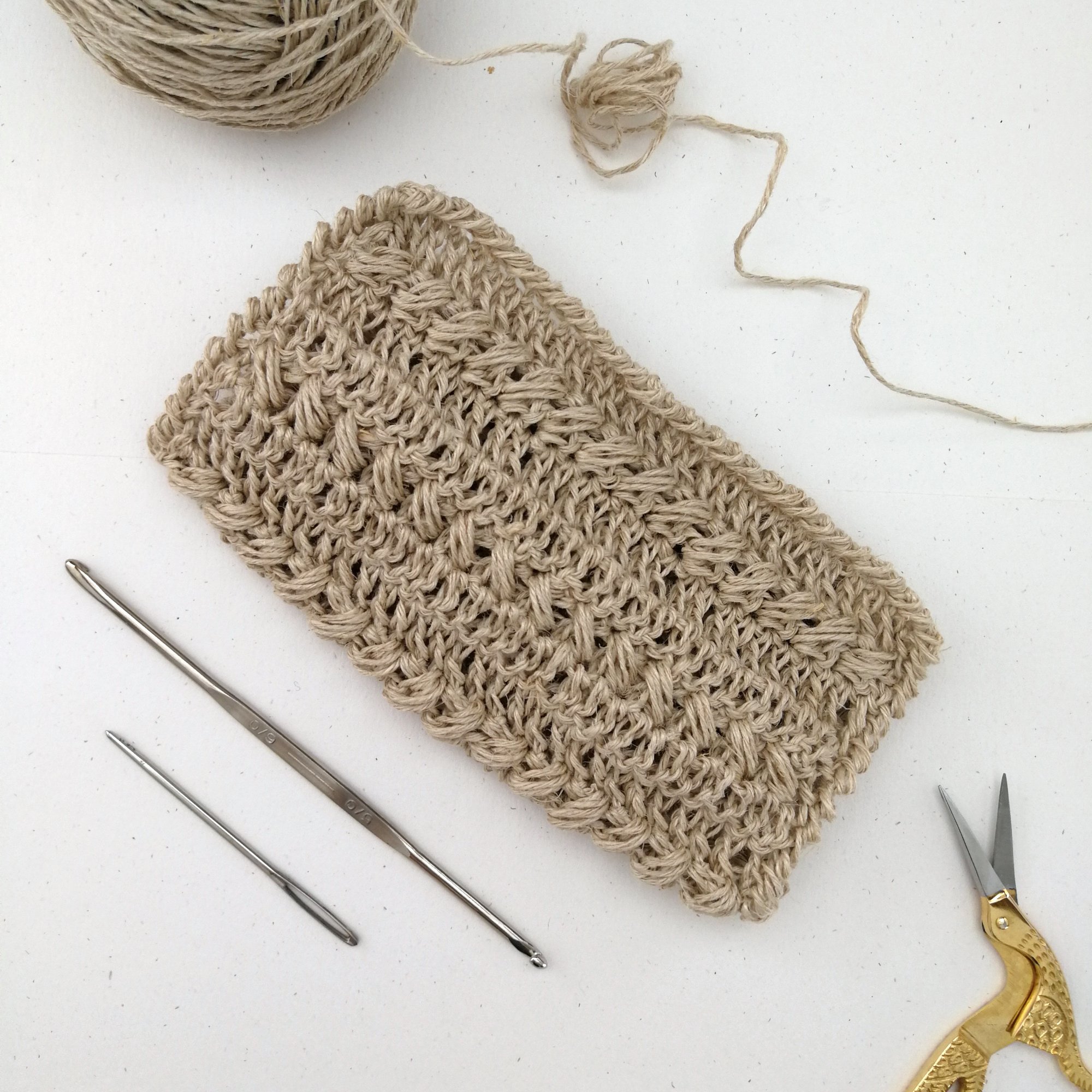 A square, textured dishcloth made with using the crochet pattern is laid out on a white table in a diamond shape. There are alternating rows of textured stitches and a textured border.