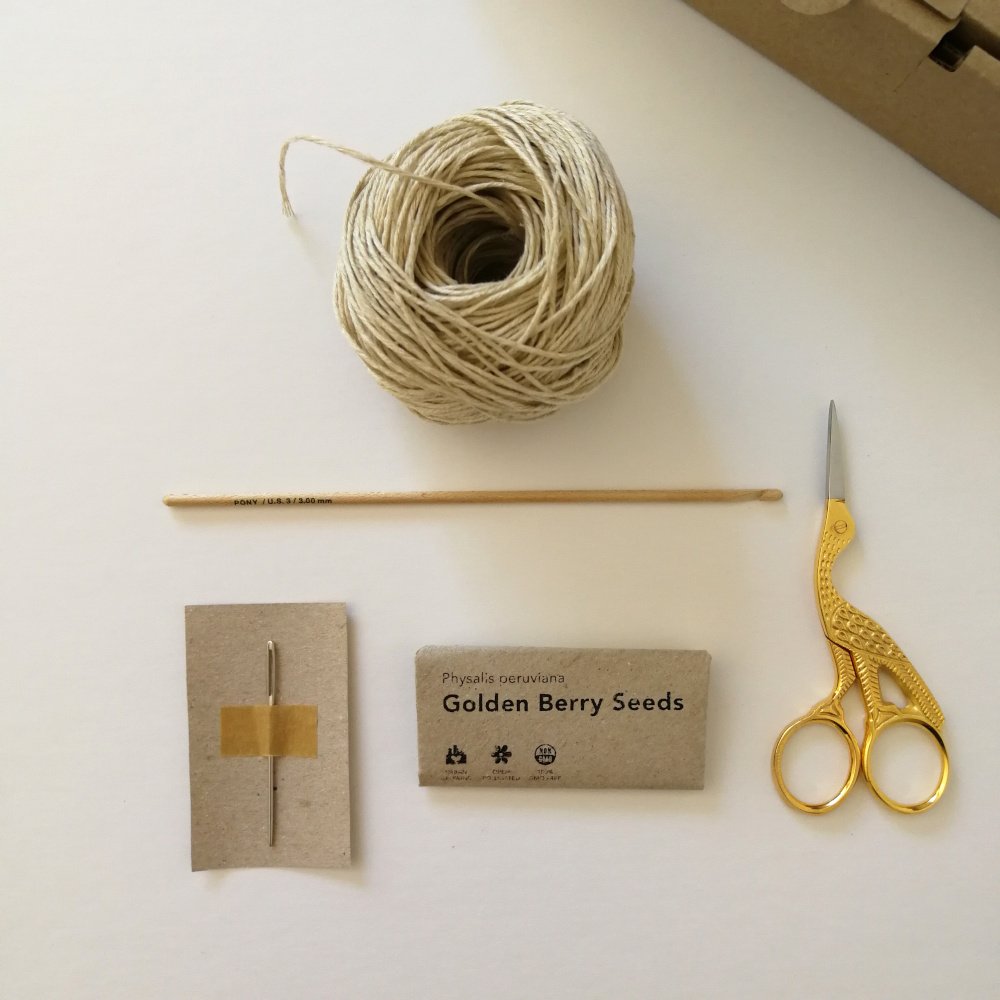 A birds eye view of the crochet notions that are included in the box. The hemp yarn, wooden crochet hook, darning needle, scissors and packet of Golden Berry seeds.