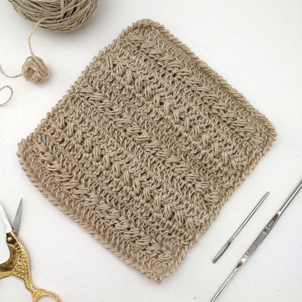 A square dishcloth is laid out on a white table in a diamond shape. There are alternating rows of textured stitches and a textured border.