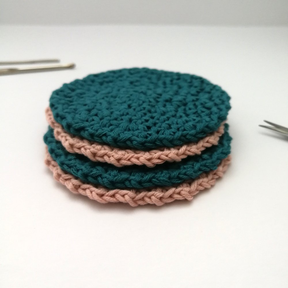 A stack of four face scrubbies are sat on a white background. The alternate in colour with teal on the top then pink, then teal and pink again at the bottom.