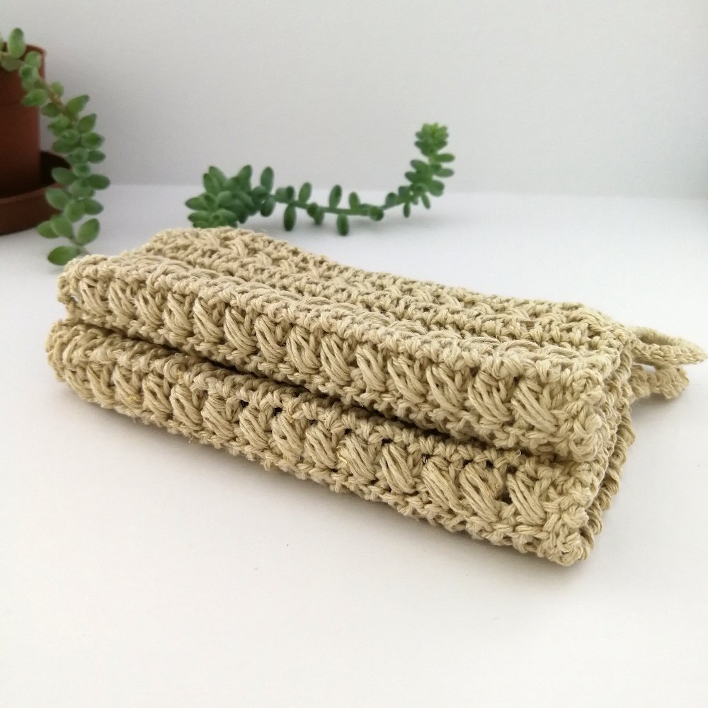 A stack of two dishcloths, folded in half on a white background with a green succulent behind. The fold in the dishcloths shows the raised row of stitches and the textured of the hemp.