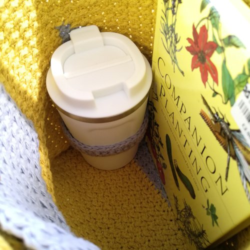 A person holding the crochet tote bag made from this pattern is stood facing left with the bag over their shoulder. The bag is mostly yellow with a grey triangle in the bottom right corner.